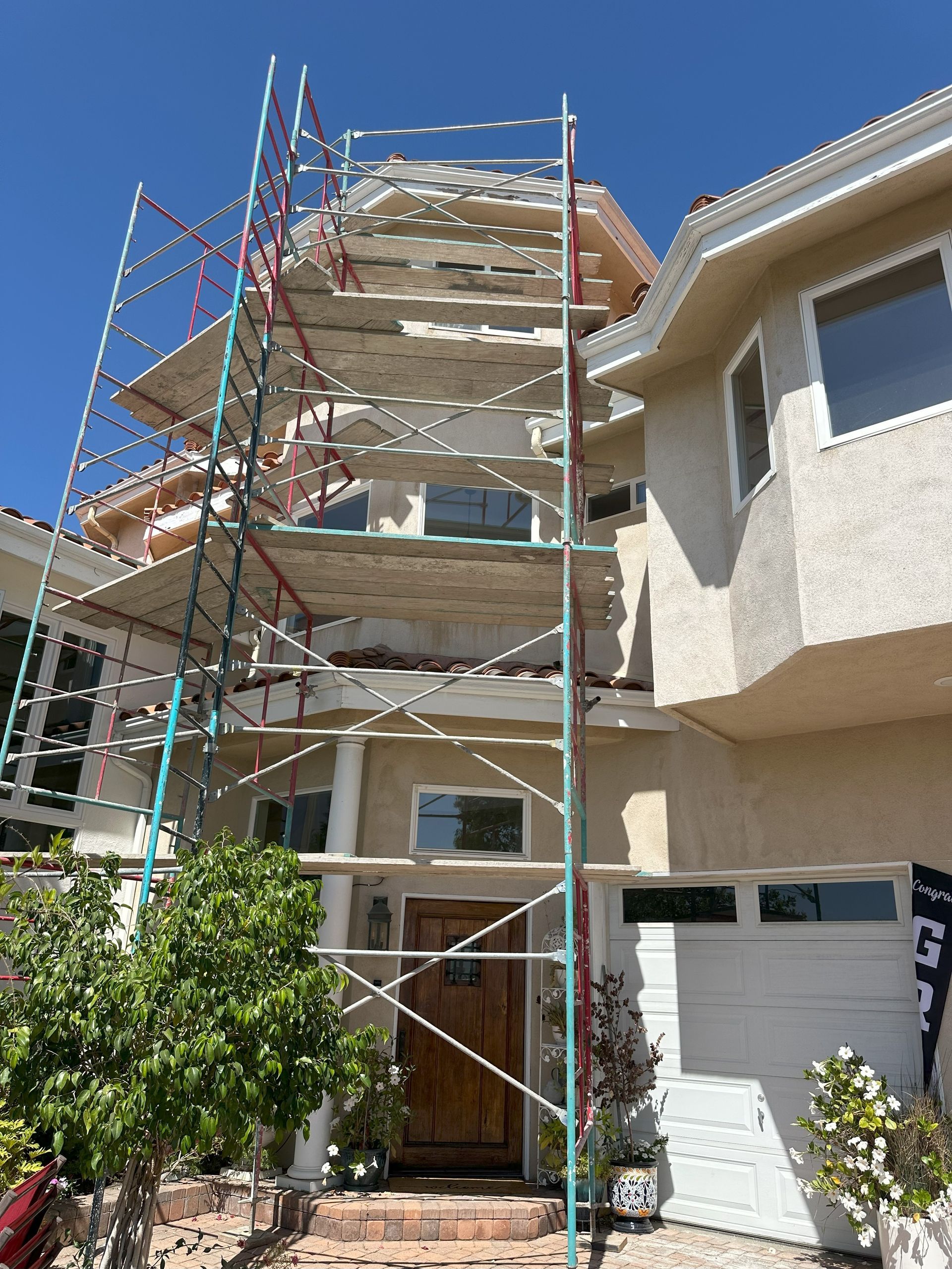 Scaffolding surrounds a two-story house for exterior work, under a clear blue sky.