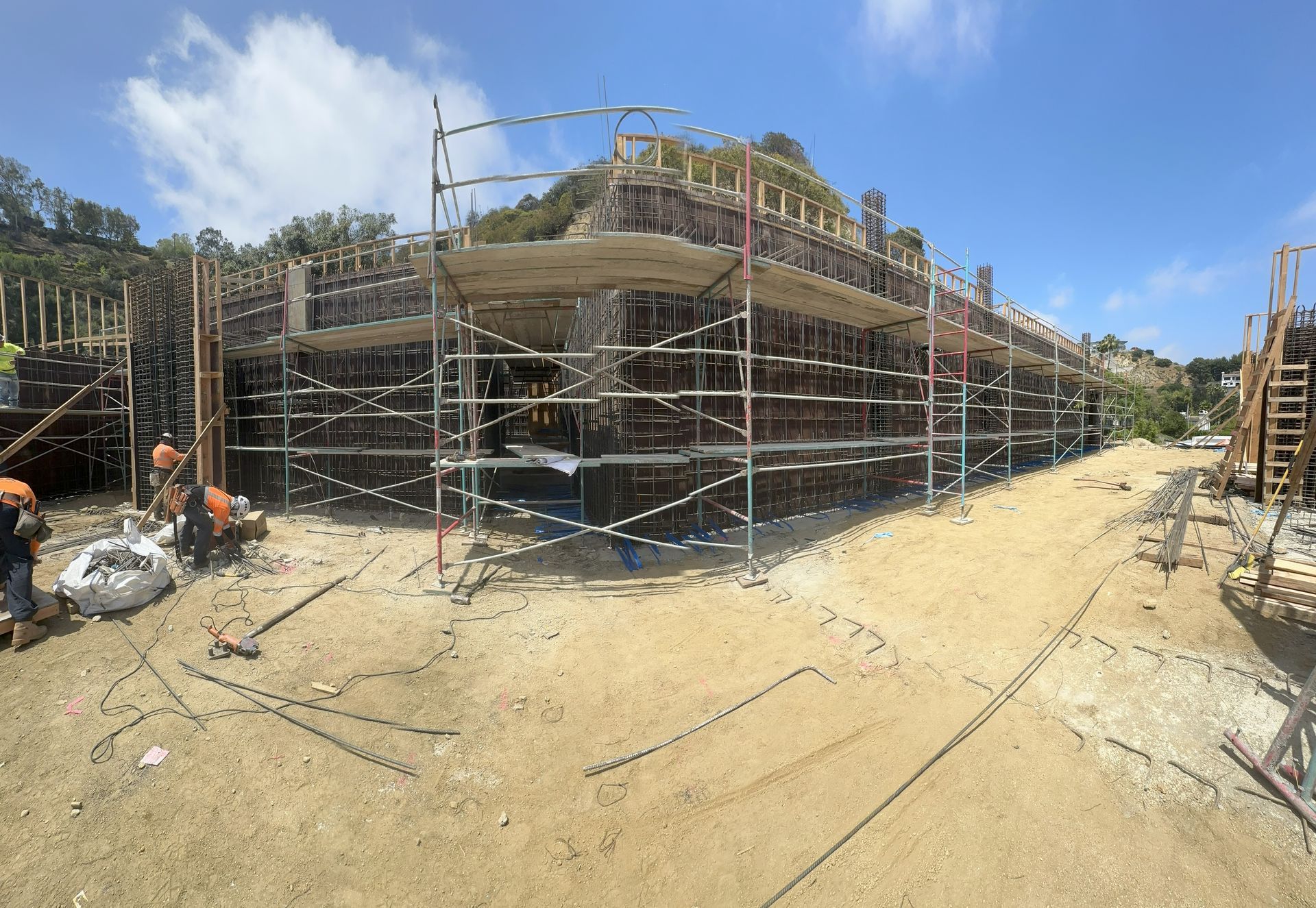 Construction site with scaffolding around a building; workers are present on a sunny day.