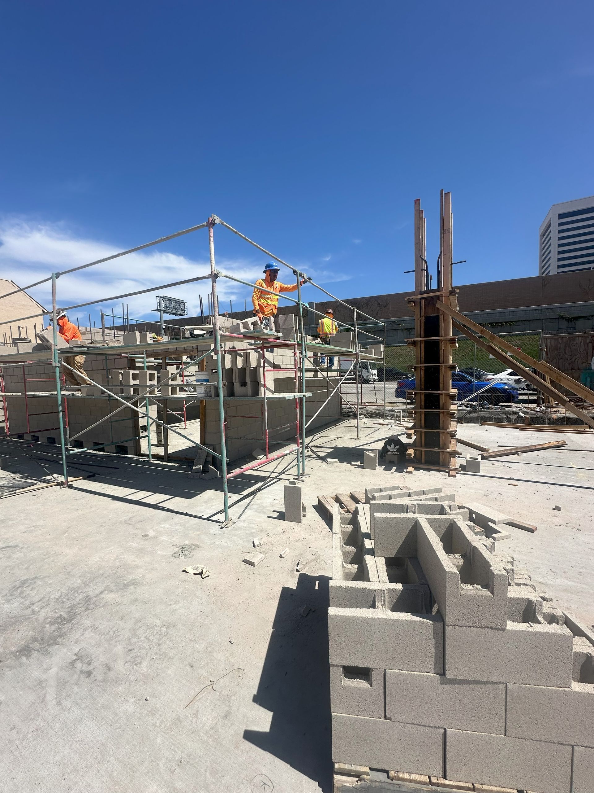 Construction site: Workers on scaffolding building with cinder blocks under a blue sky.