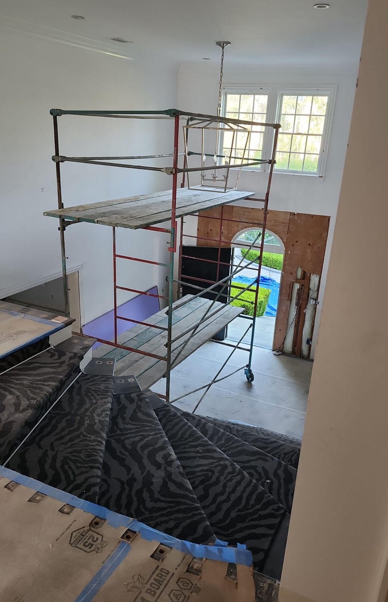 Scaffolding on staircase; construction inside a building with gray carpet, white walls, and a window.