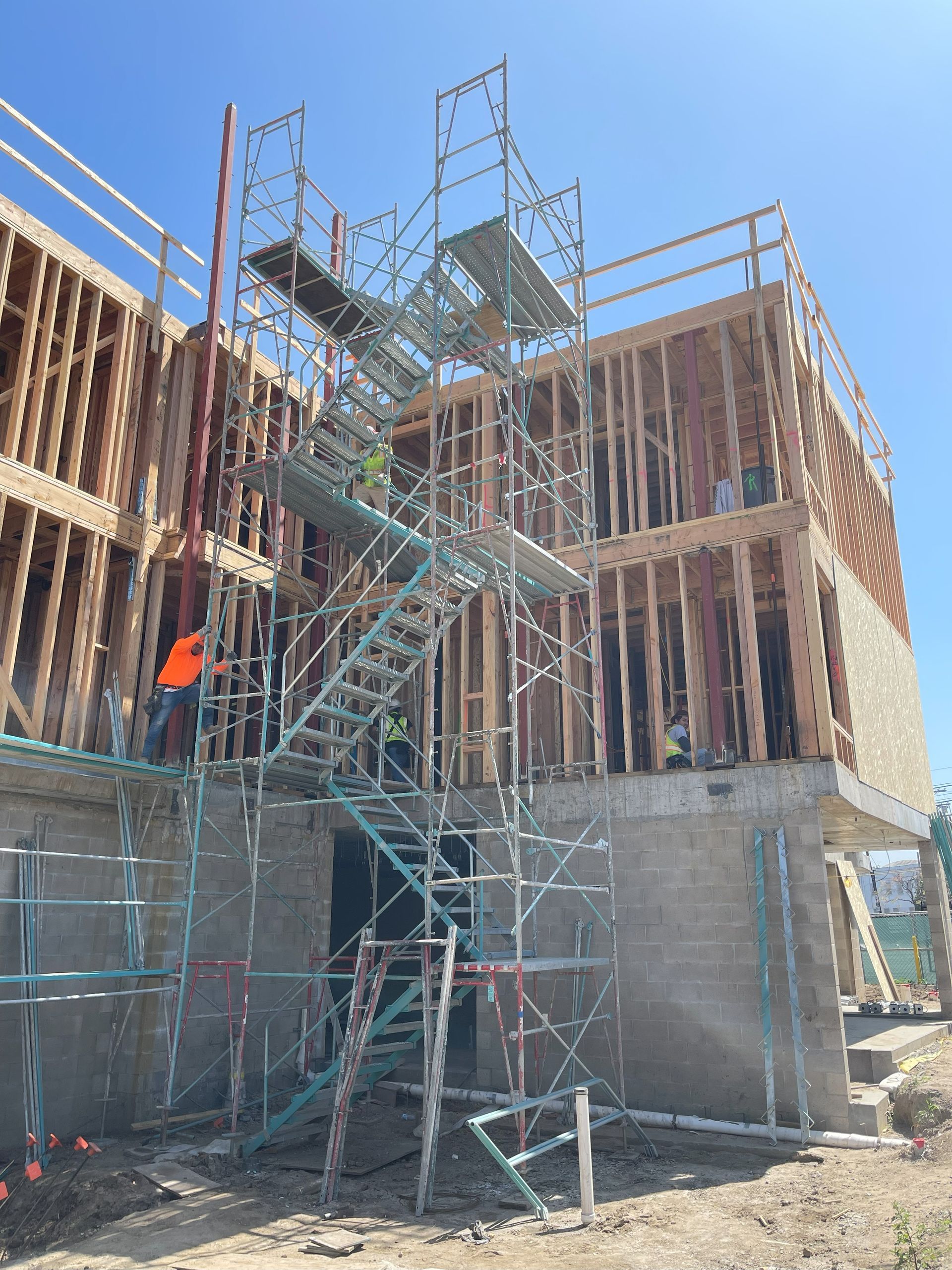Construction site with scaffolding; workers, partially built wood frame building; sunny day.