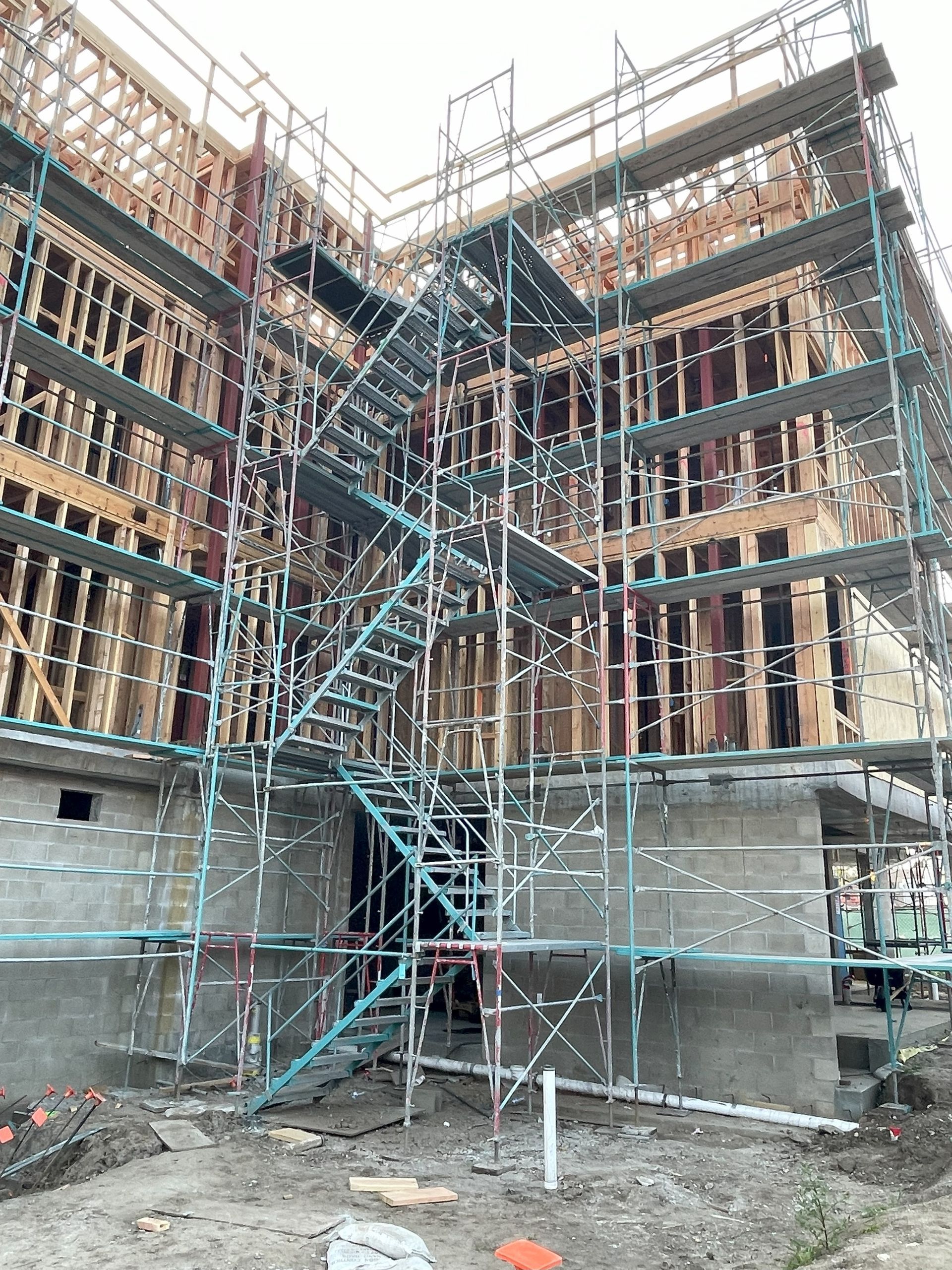 Construction site with scaffolding surrounding a multi-story wood-frame building.
