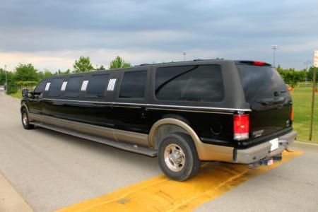Black stretch SUV limousine on a road, viewed from the rear side.
