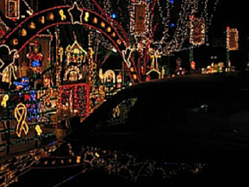 Night street with a car in front of colorful holiday light displays and archway decorations