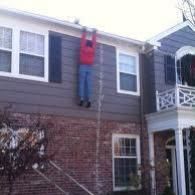 Person hanging from second-story window of a house, wearing a red shirt and jeans.