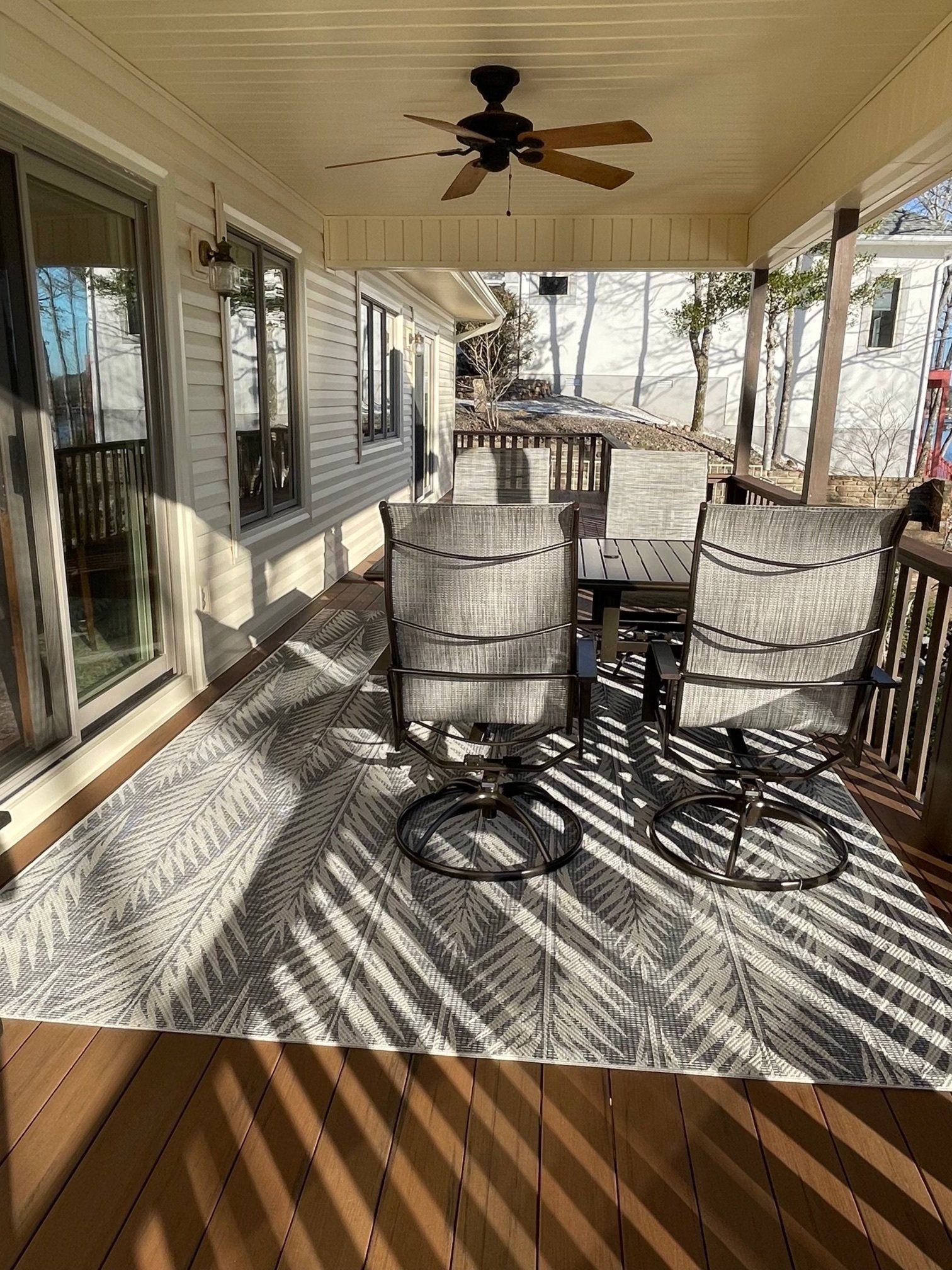 Covered outdoor deck with a rug, table, chairs, and ceiling fan.