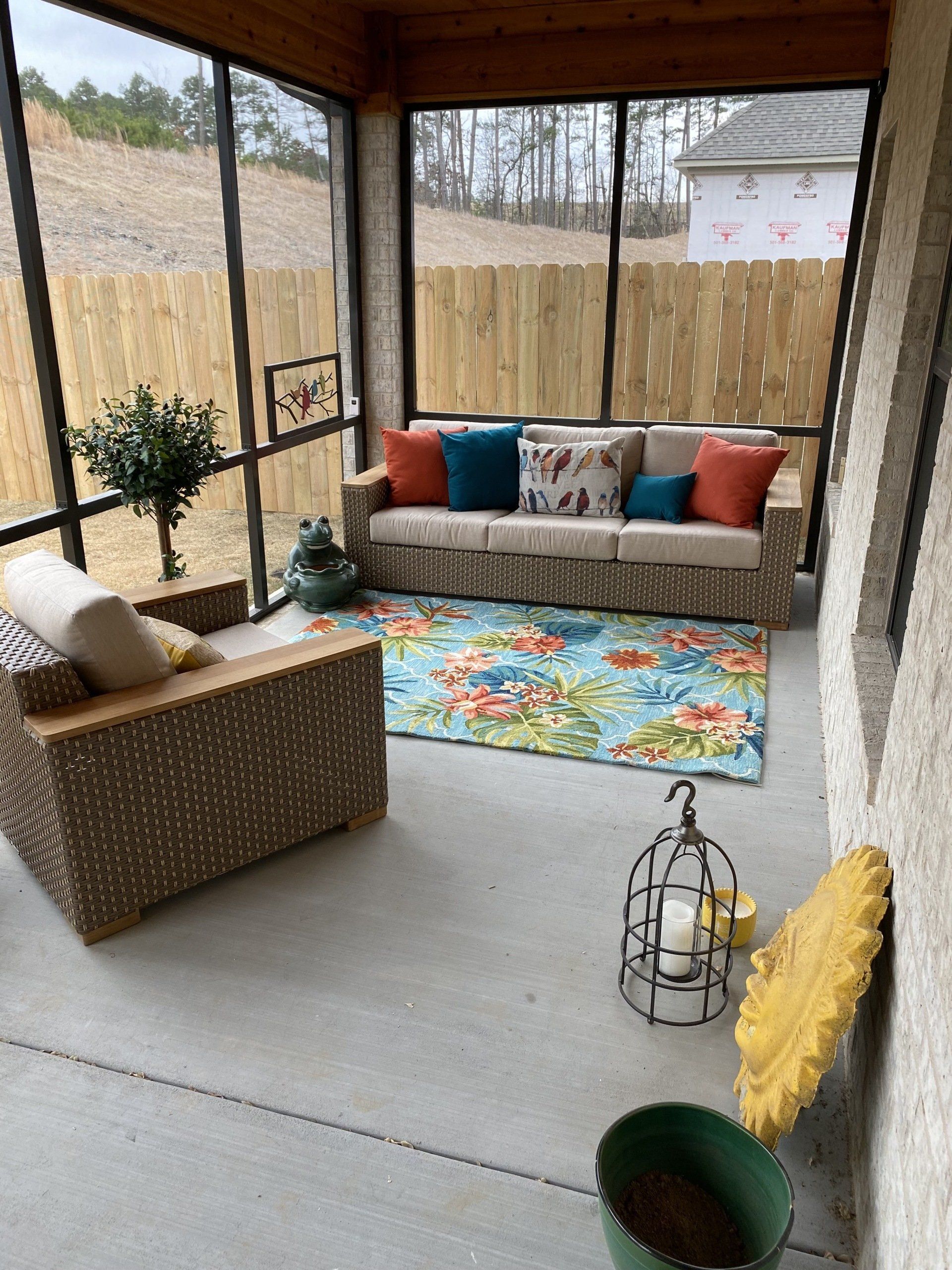 Screened porch with wicker furniture, colorful pillows, rug, and potted plants.