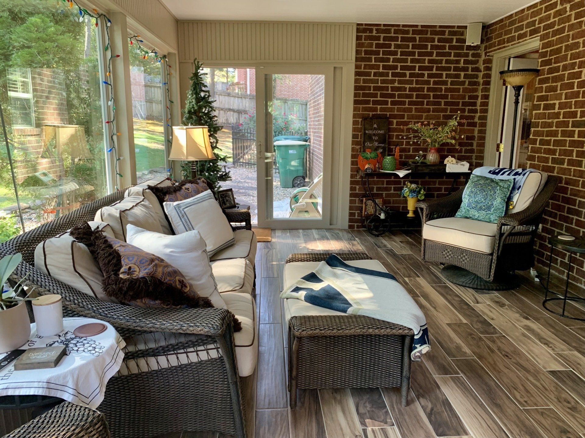 Sunroom with brick wall, wicker furniture, and a bench; doors lead outside.