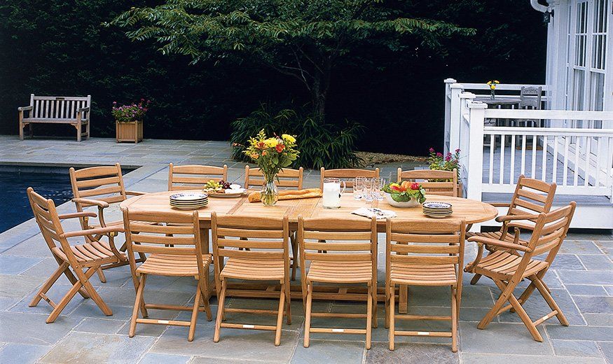 Outdoor dining set with wooden chairs around a long table, flowers, and a pool.