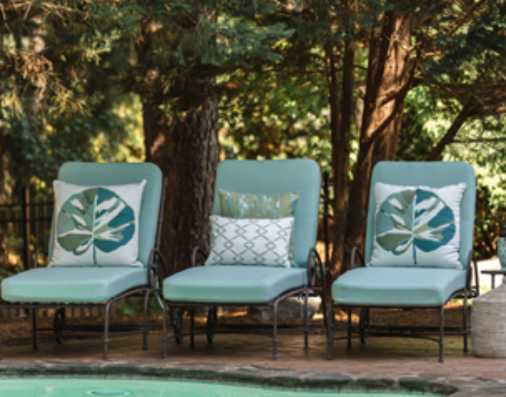 Three aqua-colored lounge chairs with leaf-print pillows by a pool, in a natural outdoor setting.