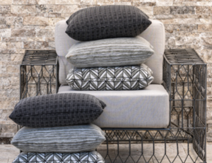 Stack of gray and patterned pillows on a light gray chair against a stone wall.