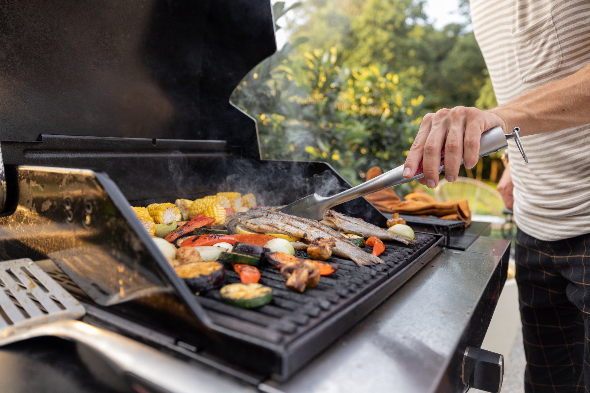 Person grilling vegetables and fish on a barbecue.