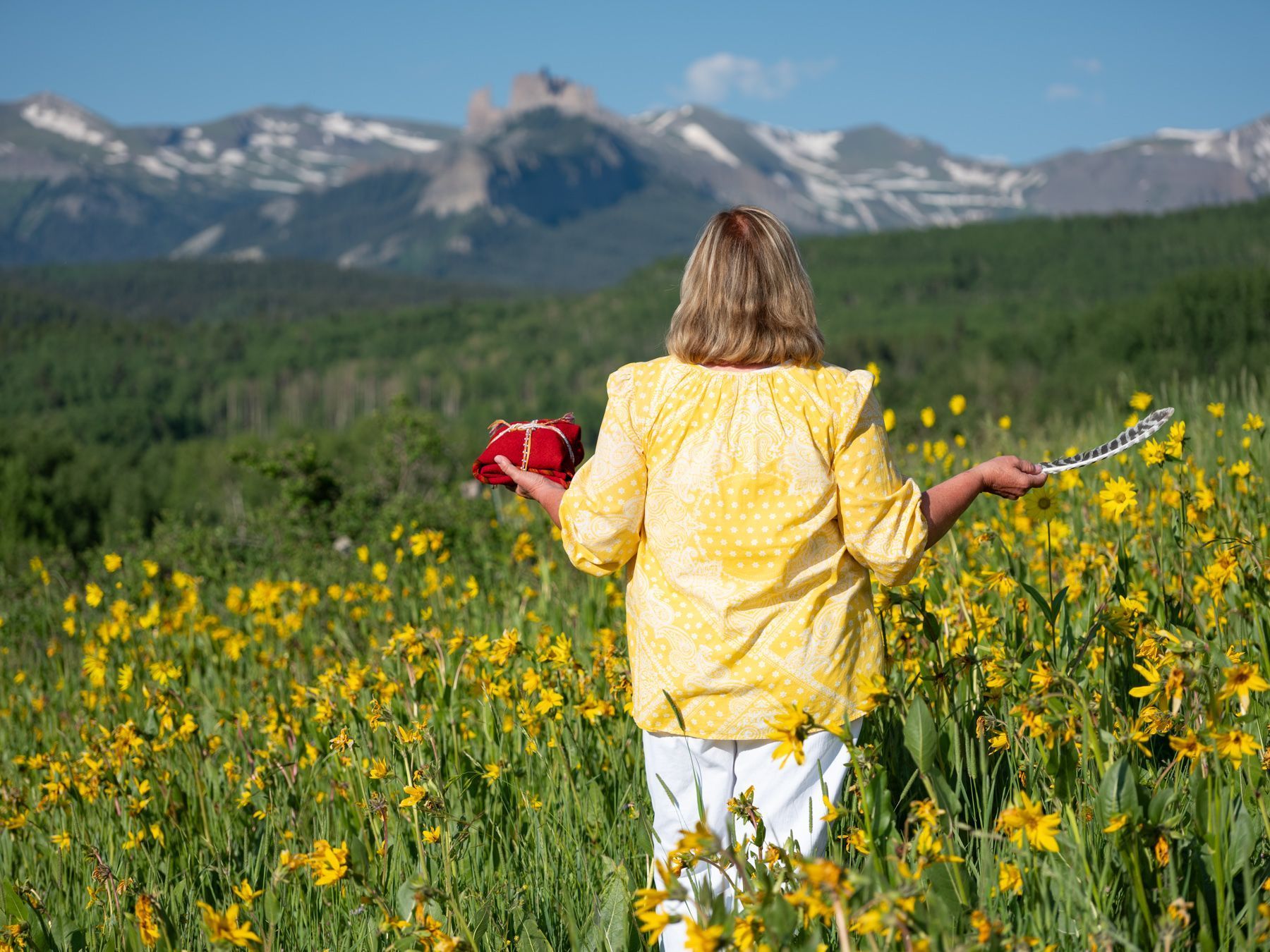 A woman in a yellow shirt is walking through a field of yellow flowers.