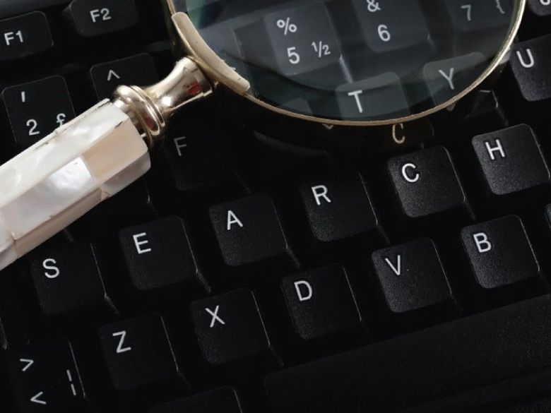 Een vergrootglas boven een zwart computertoetsenbord, waarbij de toetsen met letters en symbolen worden gemarkeerd.