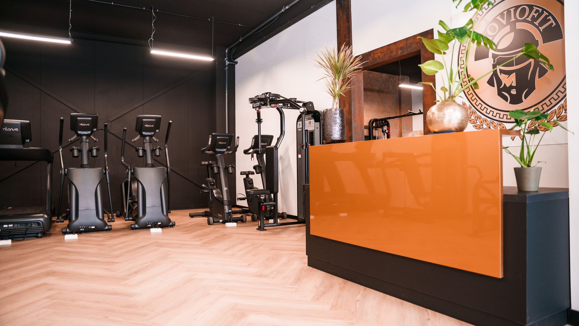 Een fitnessruimte met een receptie en veel fitnessapparatuur.