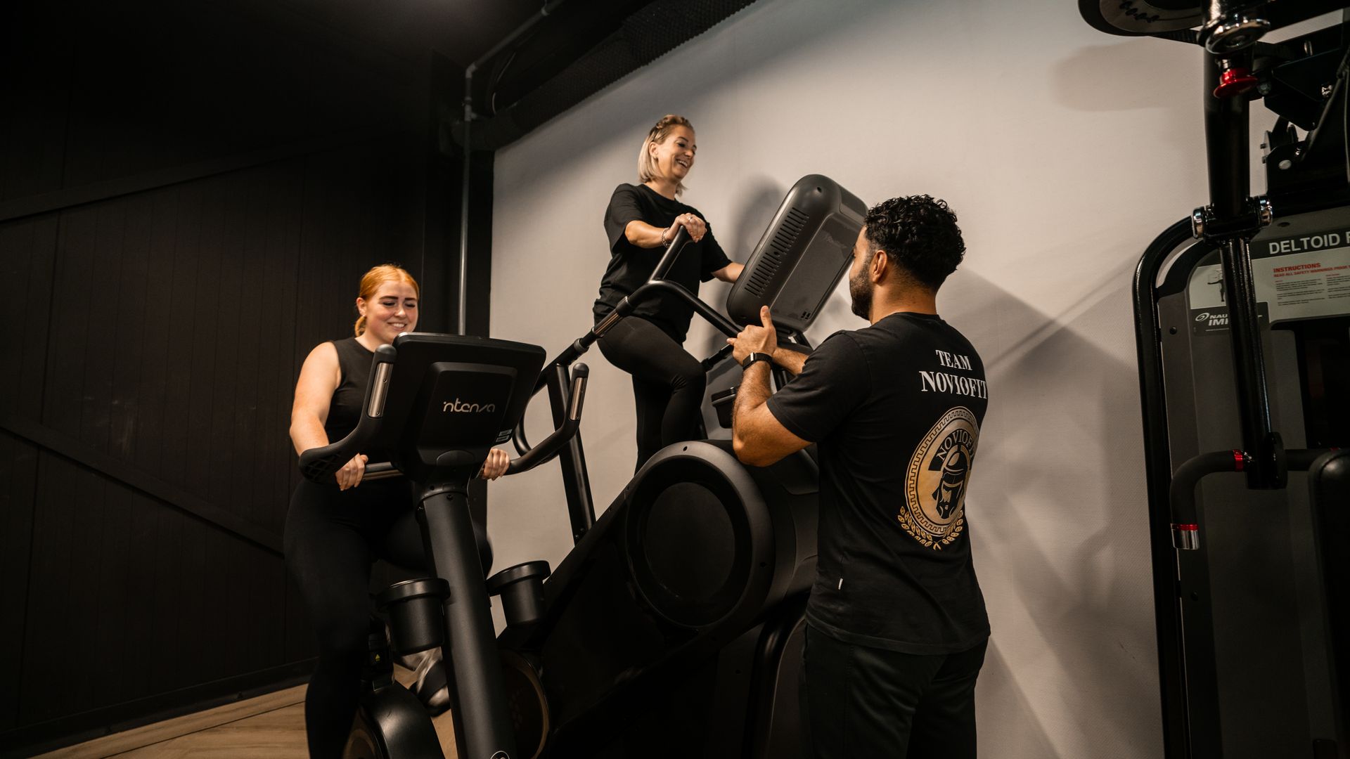 People exercising on stationary bikes in a dim studio, with one person instructing another.