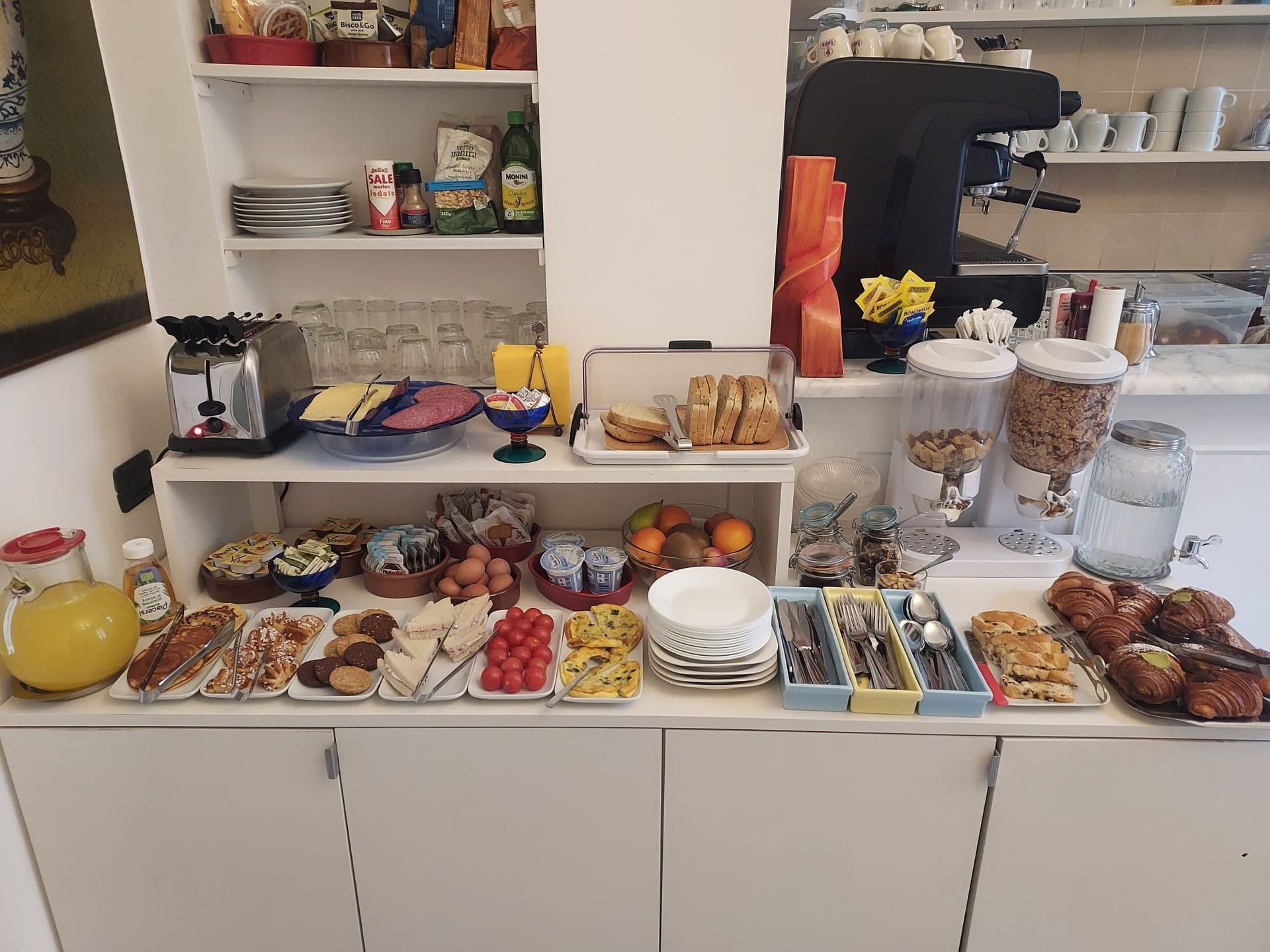 Dessert buffet with cakes, pastries, fruit, and coffee on a white counter in a kitchen or café.