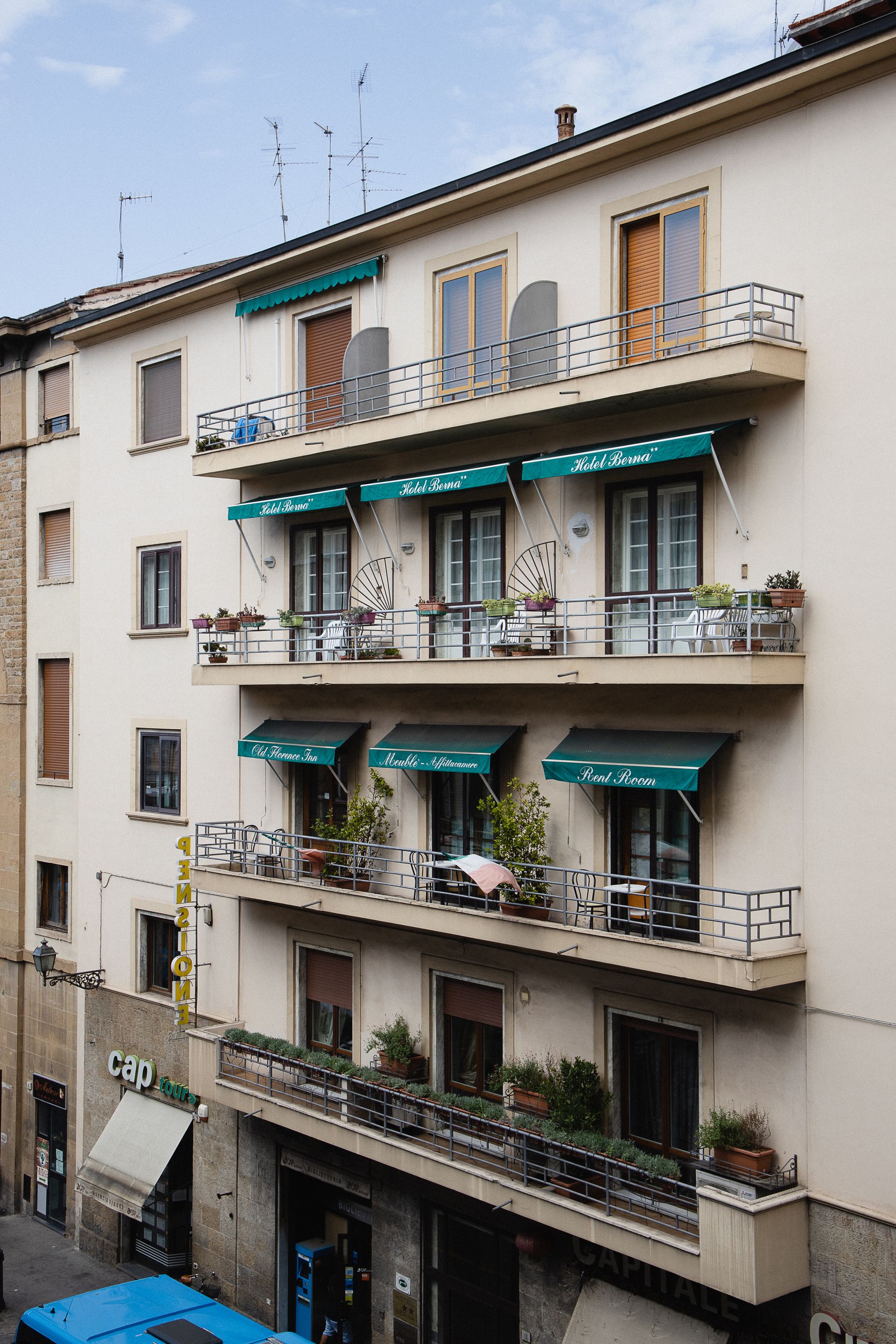 Multi-story apartment building with balconies, teal awnings, and potted plants on a city street