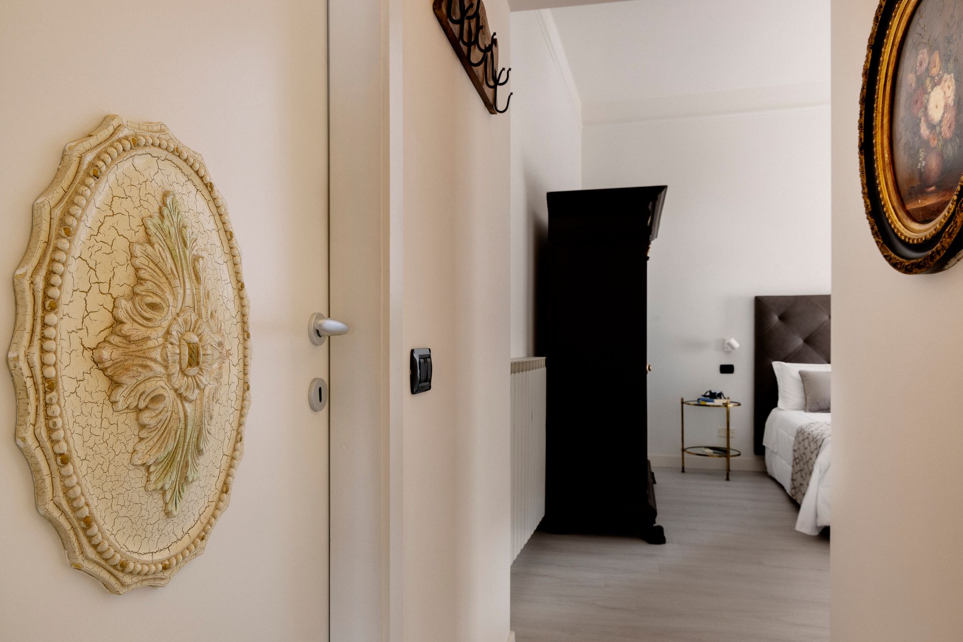 Elegant hallway with decorative wall plaques, a black cabinet, and a glimpse of a bedroom through an open door