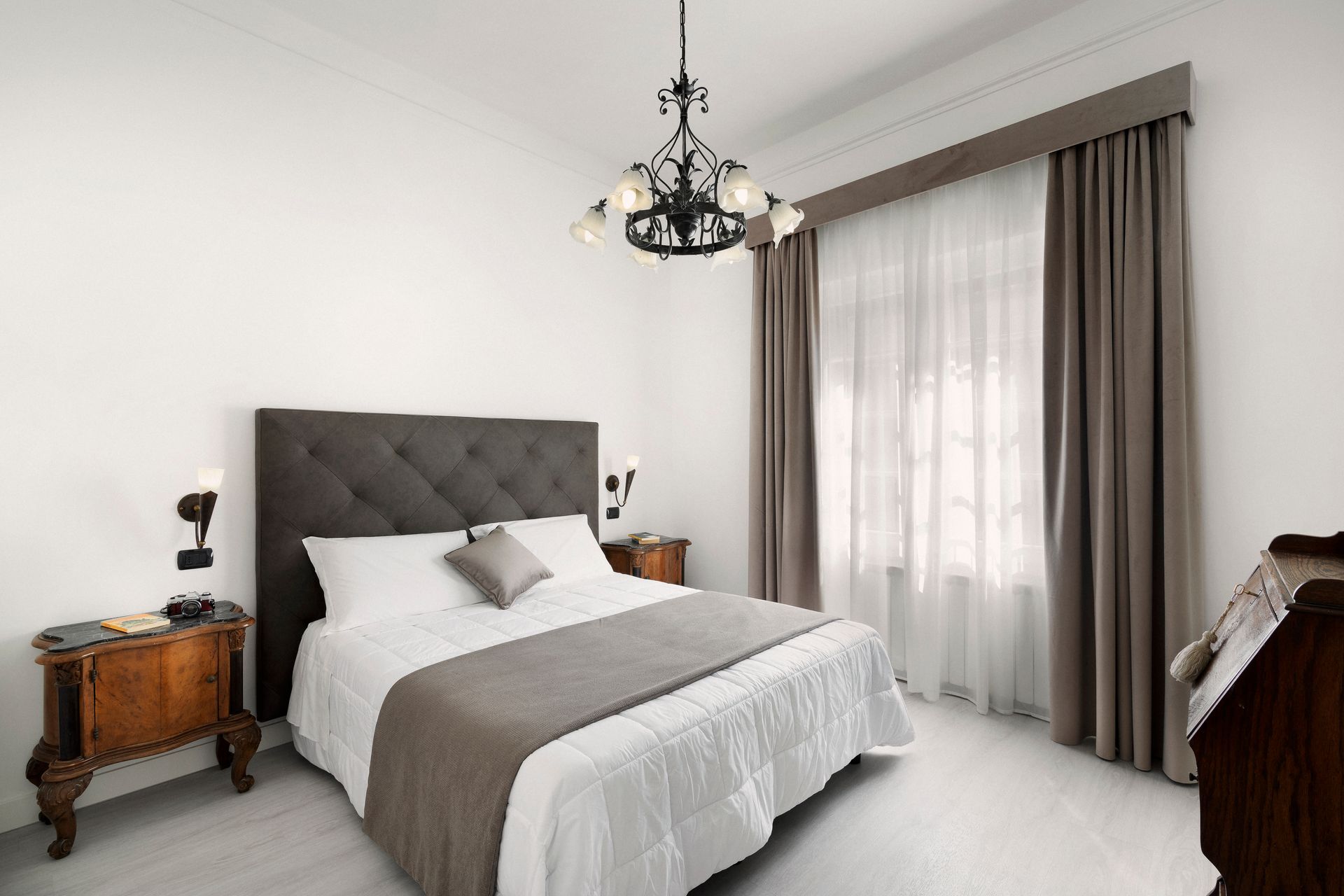 Elegant bedroom with a tufted bed, bedside tables, chandelier, and sheer curtains by a large window