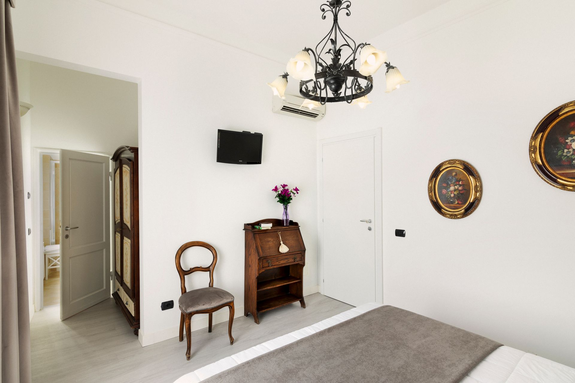 Bright white bedroom with chandelier, armoire, chair, wall art, and hallway doorway