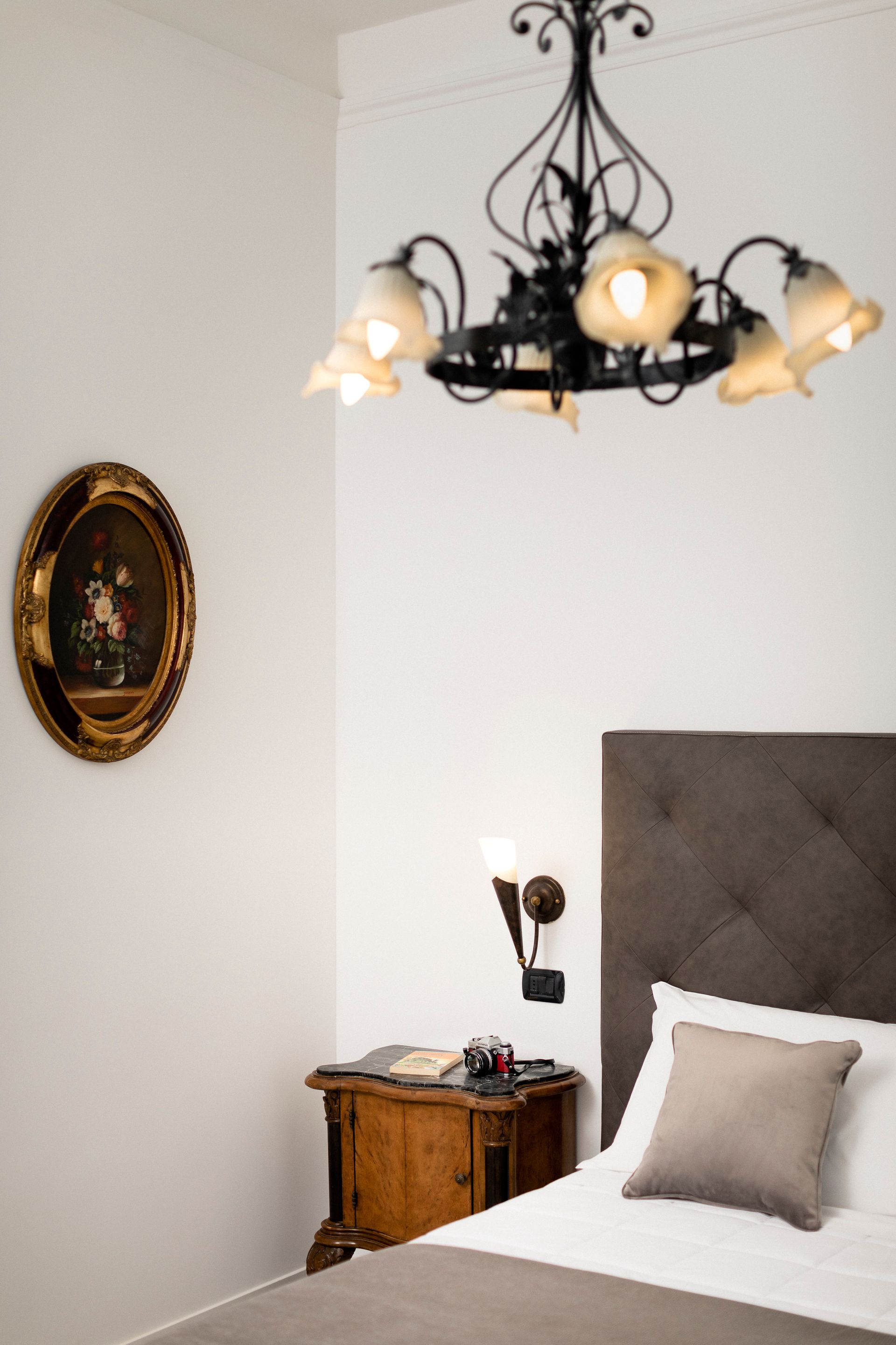 Elegant bedroom with a tufted headboard, ornate chandelier, and framed wall art