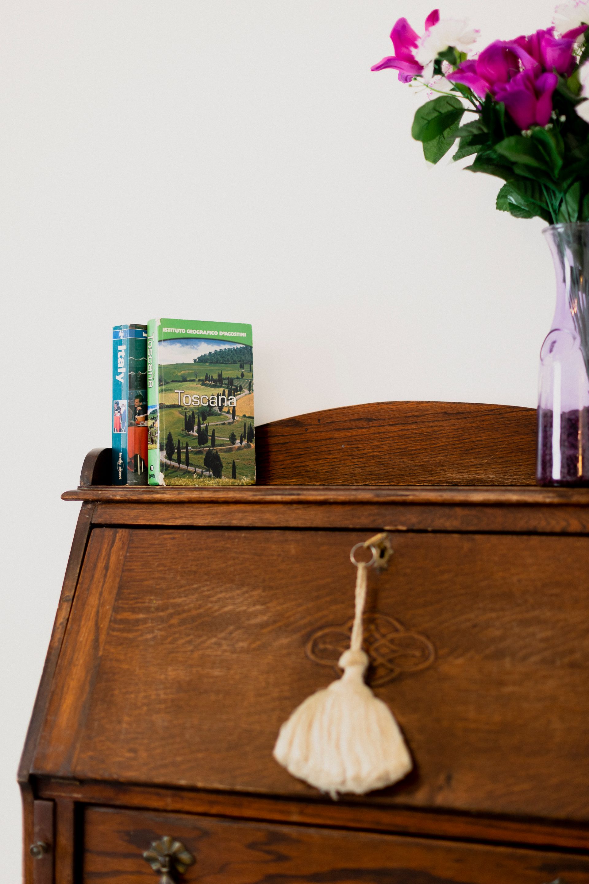 Wooden desk with books and a vase of purple flowers against a white wall
