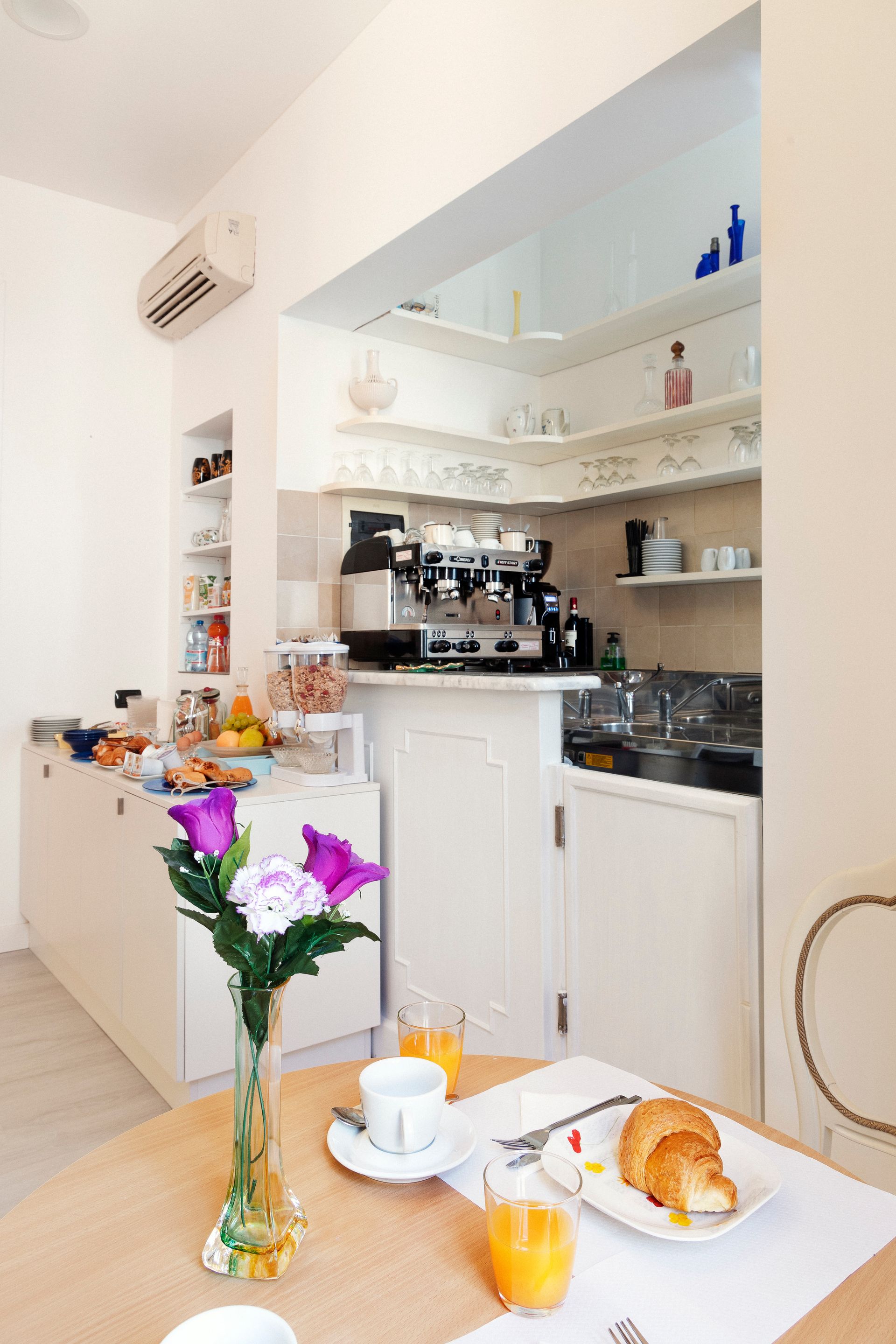 Bright cafe corner with coffee machine, flowers, and a pastry and orange juice on a table