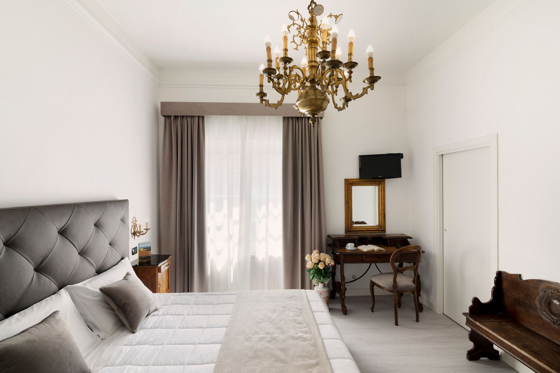 Elegant white bedroom with tufted bed, gold chandelier, curtains, desk, and bench