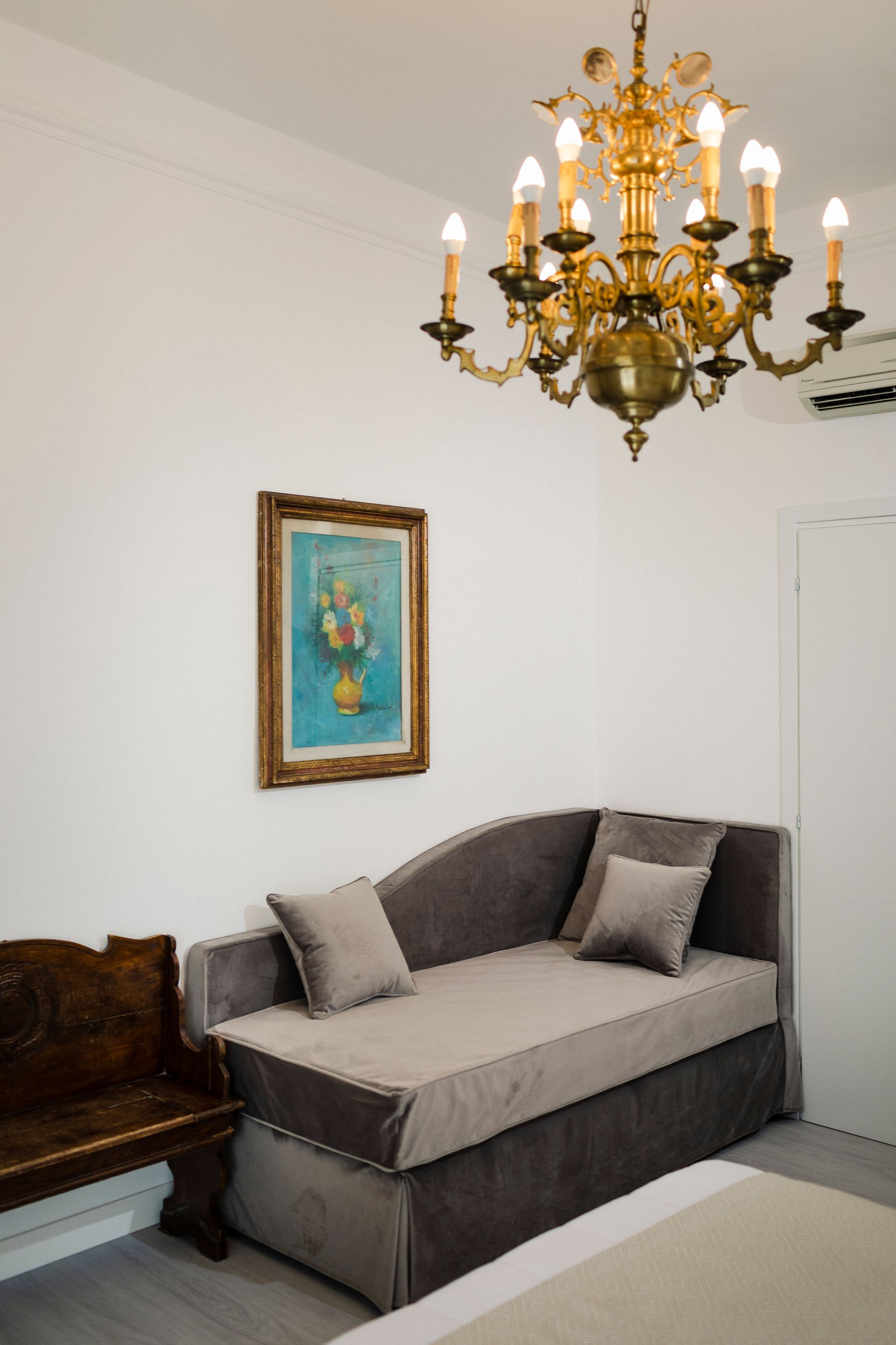 Elegant living room with gold chandelier, gray sofa, framed art, and dark wood chair against white walls