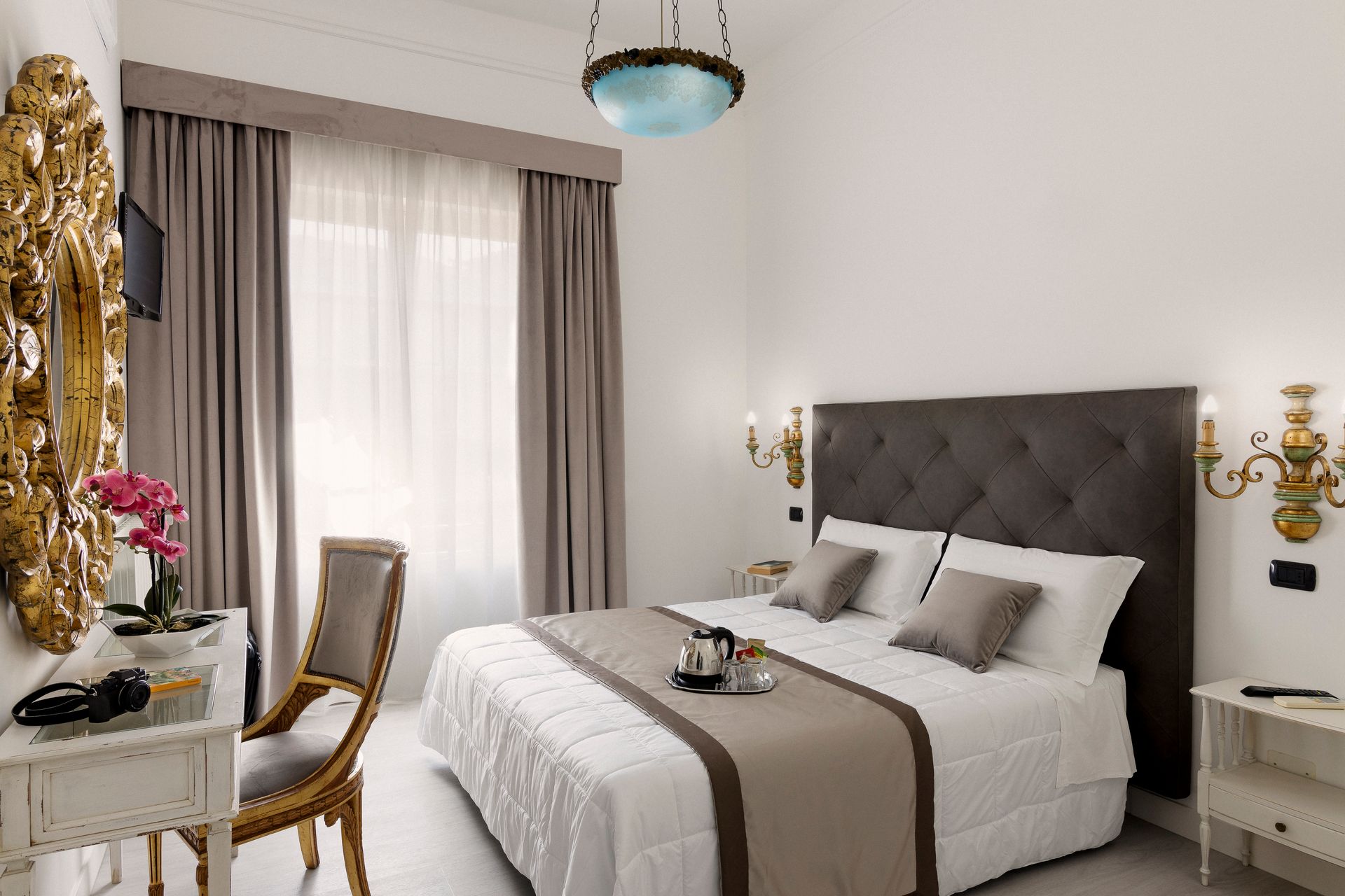 Elegant bedroom with a gray tufted headboard, white bedding, and soft curtains by a bright window.