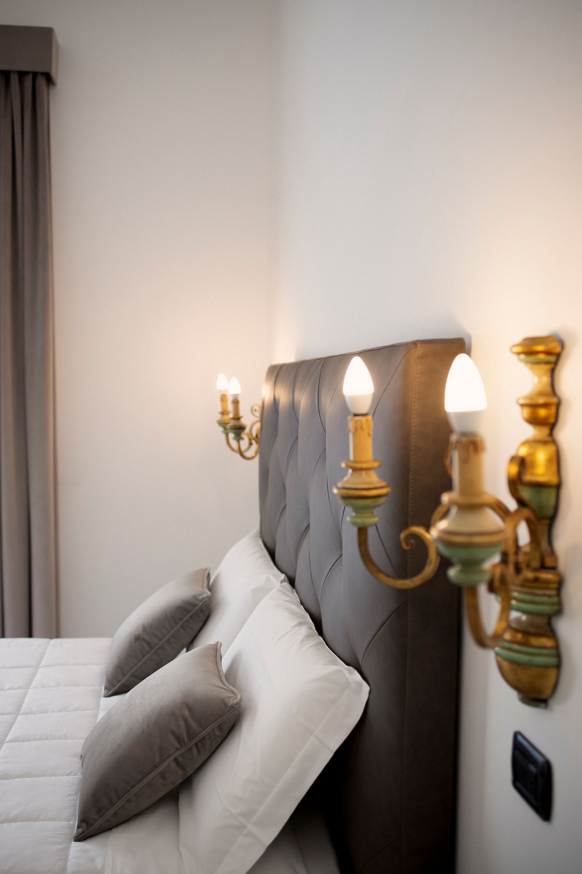 Elegant bedroom with gray upholstered headboard, white bedding, and brass wall sconces on a light wall