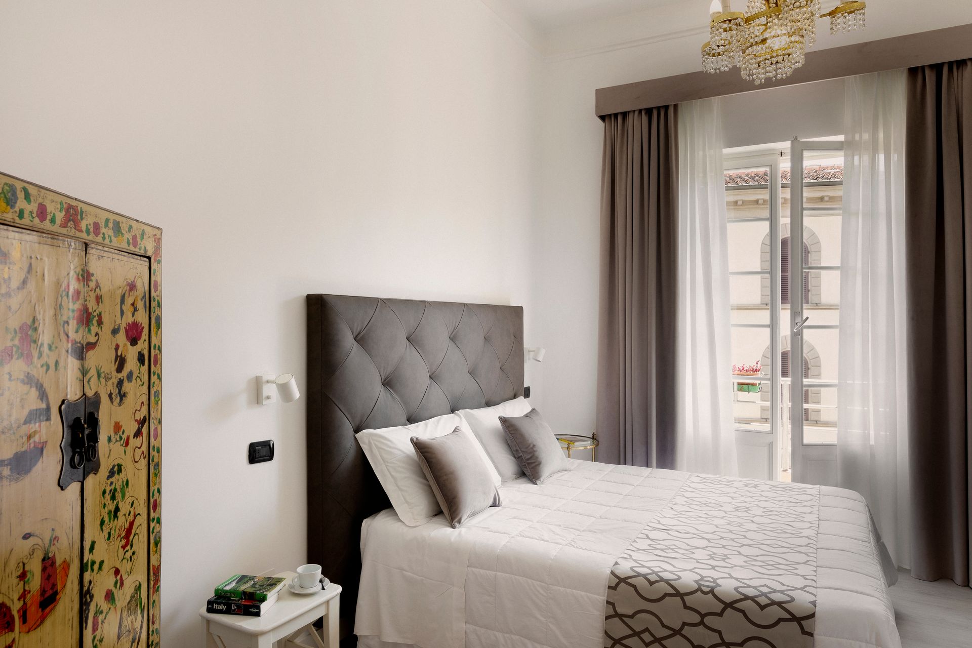 Bright bedroom with tufted gray bed, white bedding, sheer curtains, and a large window.