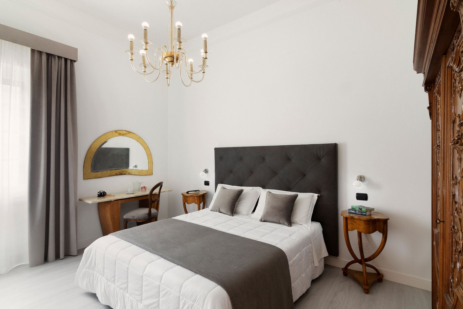 Bright bedroom with a dark headboard, white bedding, chandelier, vanity, and curtains