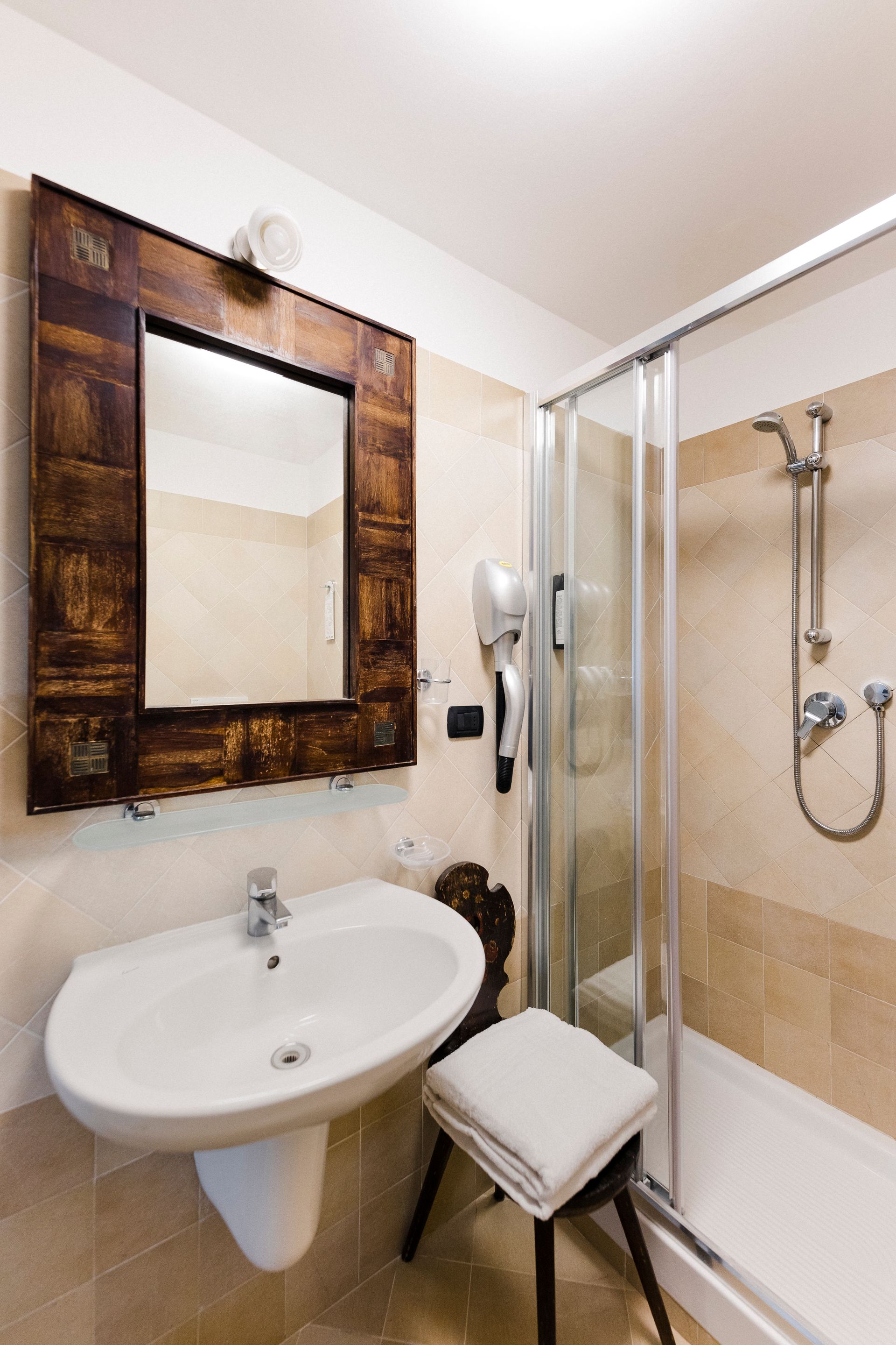 Small bathroom with sink, mirror, shower, and white stool beside the tub.