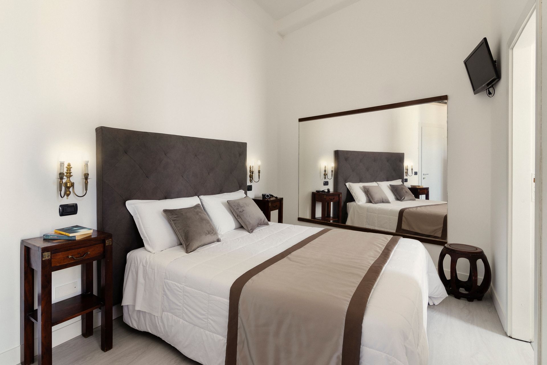 Bright bedroom with bed, gray headboard, striped blanket, bedside tables, and wall mirror.