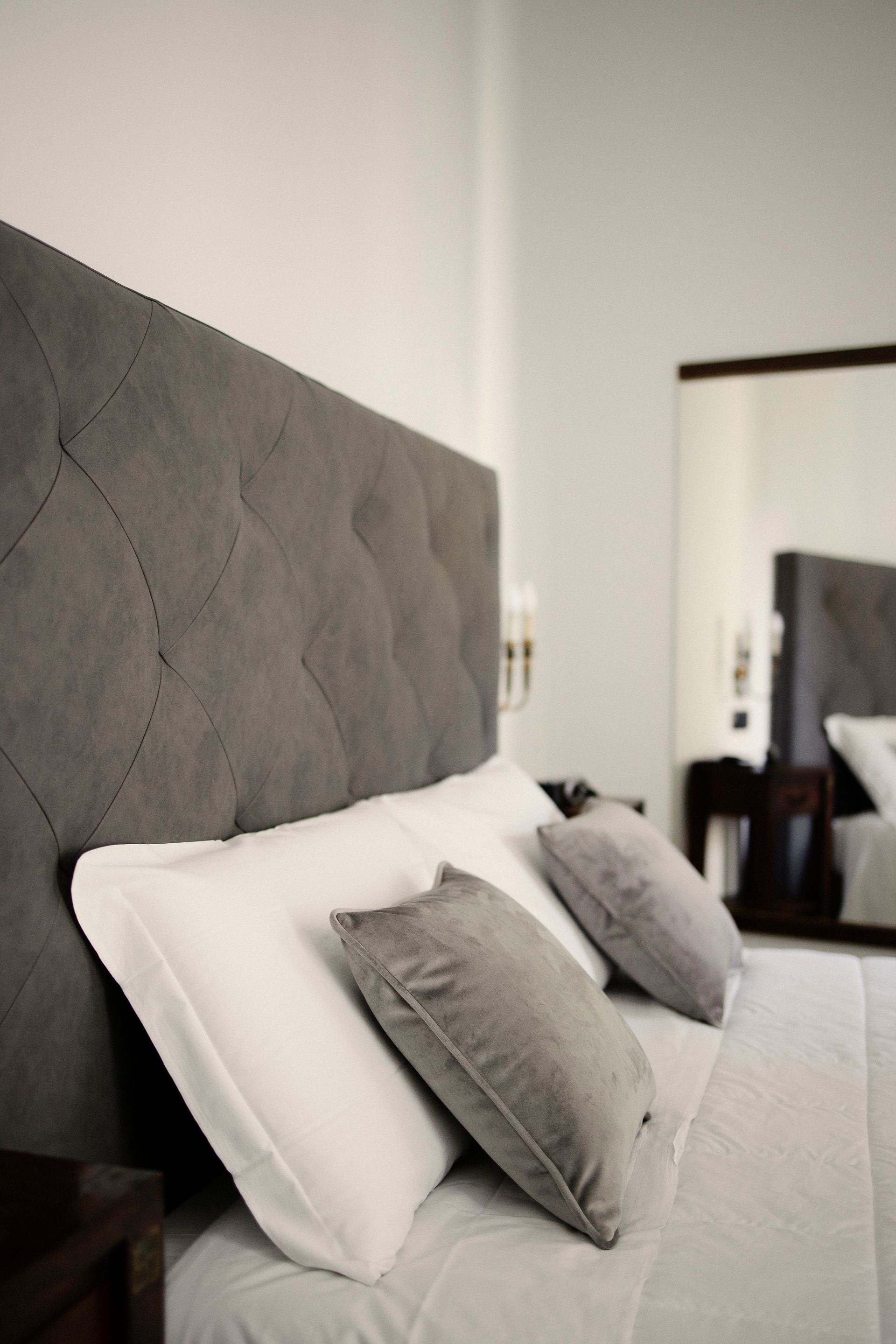 Gray upholstered headboard with white bedding and gray accent pillows in a bedroom.