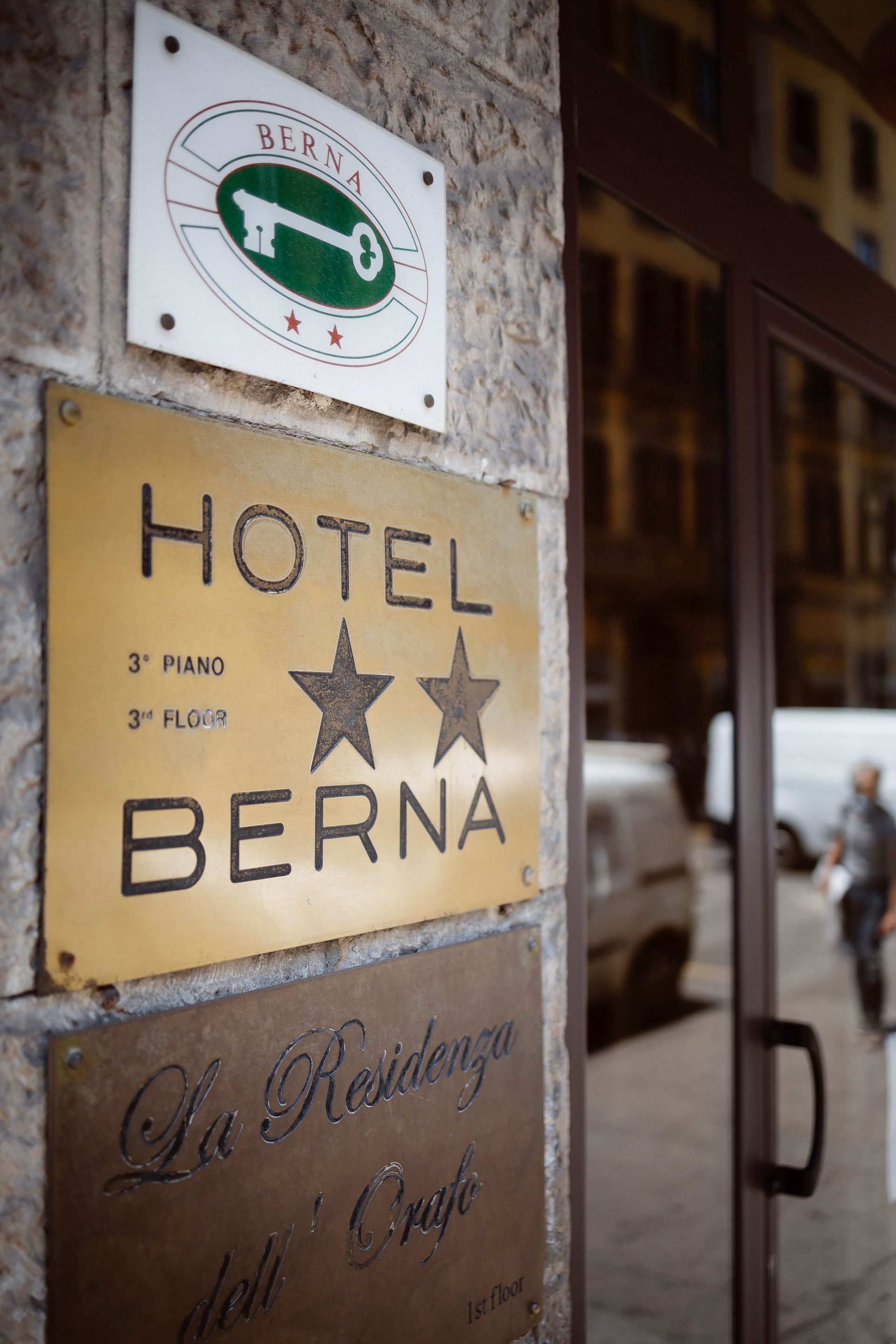 Hotel Berna sign on a stone wall with two stars and a green circular logo nearby