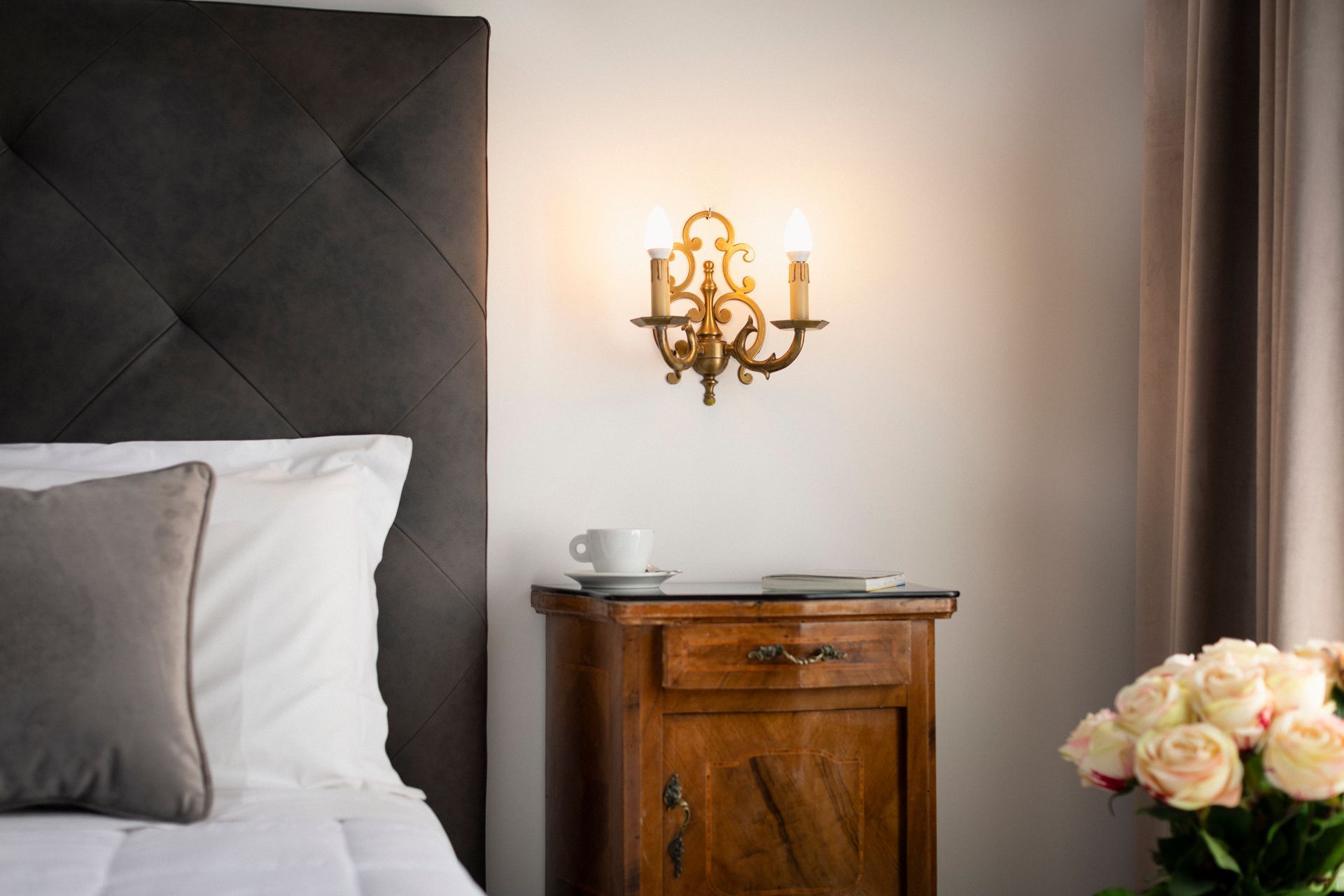 Elegant bedroom with bed, wooden nightstand, wall sconce, and a vase of flowers