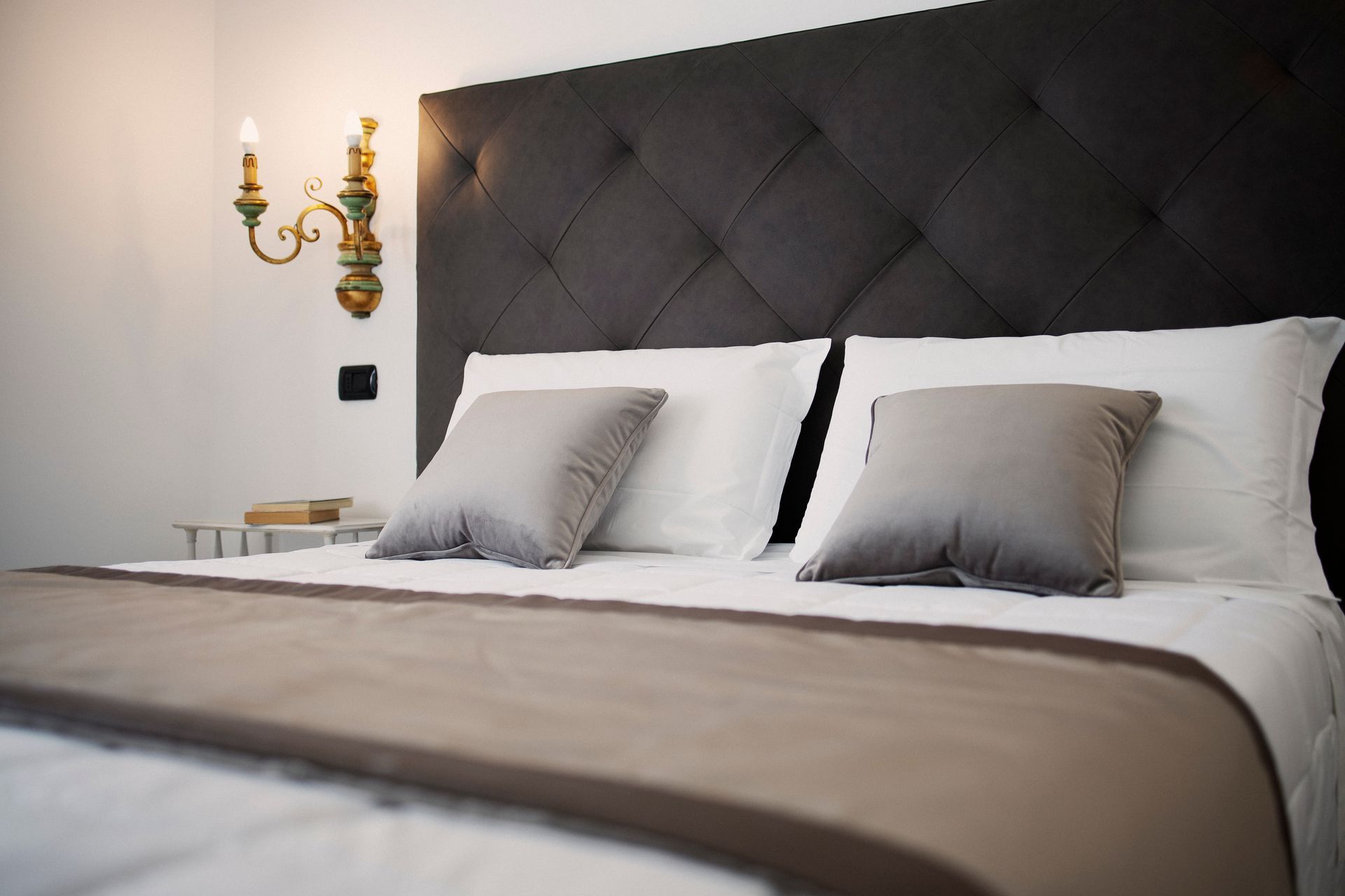 Dormitorio moderno con cabecero tapizado oscuro, ropa de cama blanca y cojines decorativos grises.