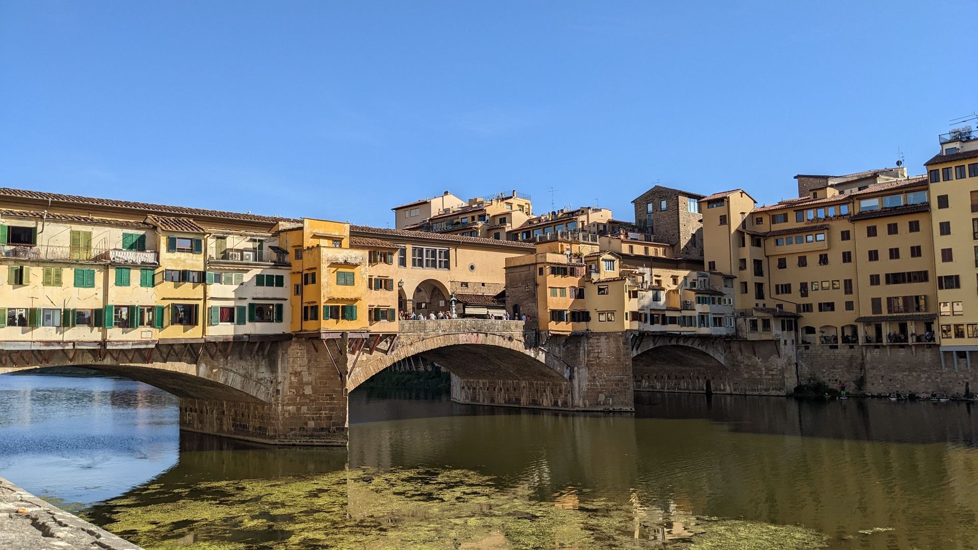 Stone bridge over a river with colorful historic buildings lining the banks in bright daylight