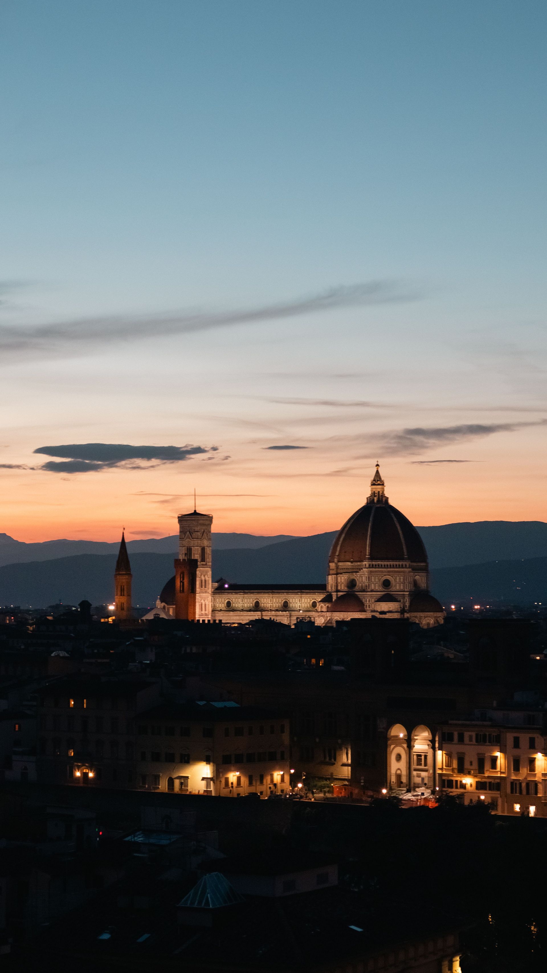 Horizonte urbano al atardecer con una catedral abovedada y una torre recortadas contra un cielo rosa azulado.