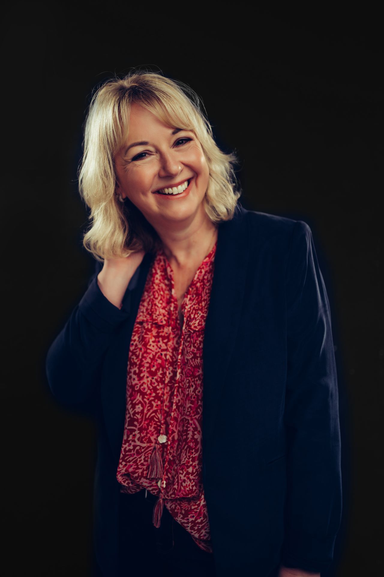 A woman in a black jacket and red blouse is smiling.
