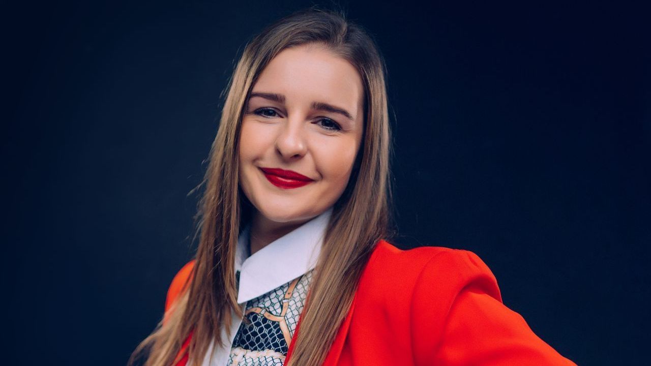 A woman in a red jacket and tie is smiling for the camera.