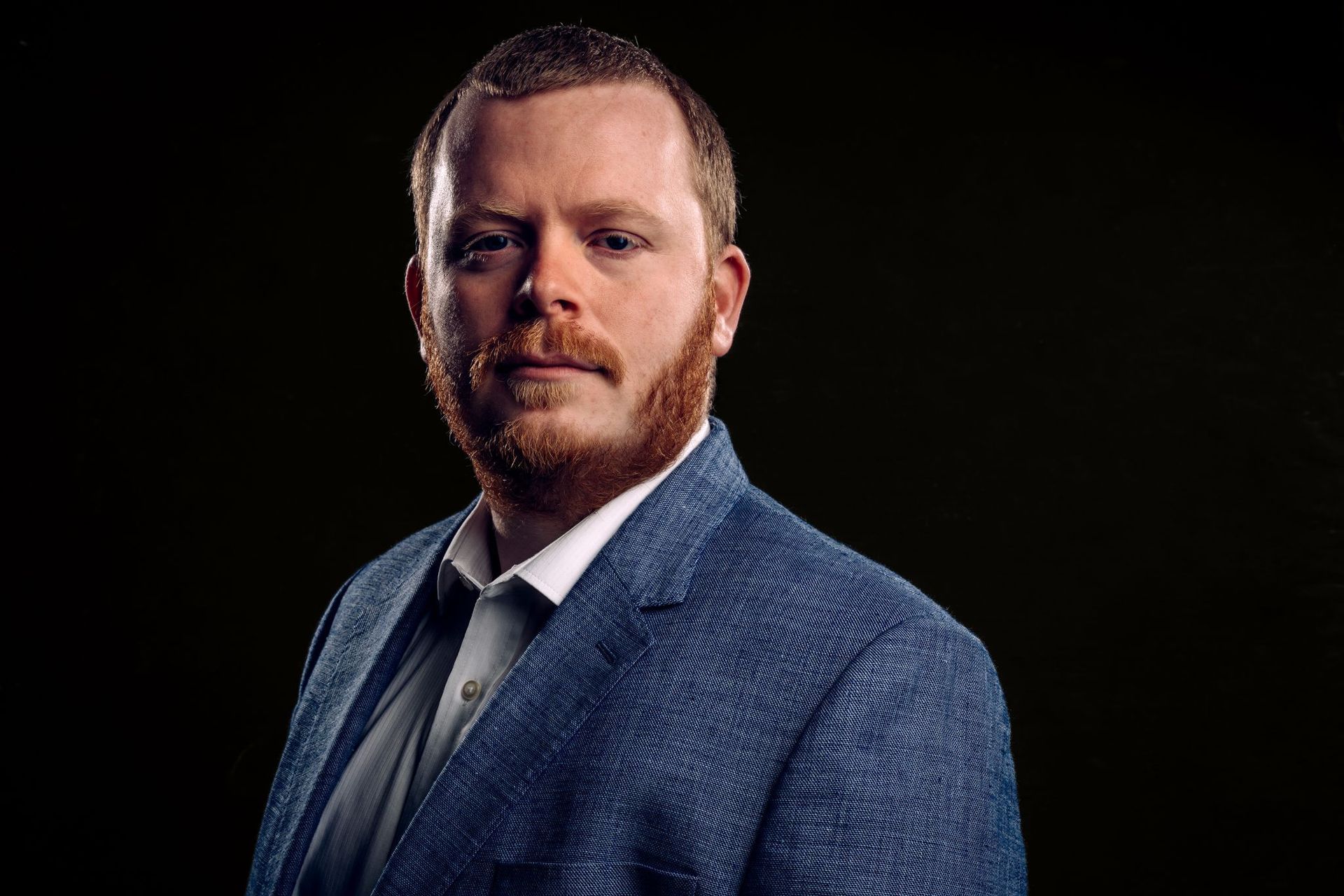 A man with a beard is wearing a blue suit and tie.