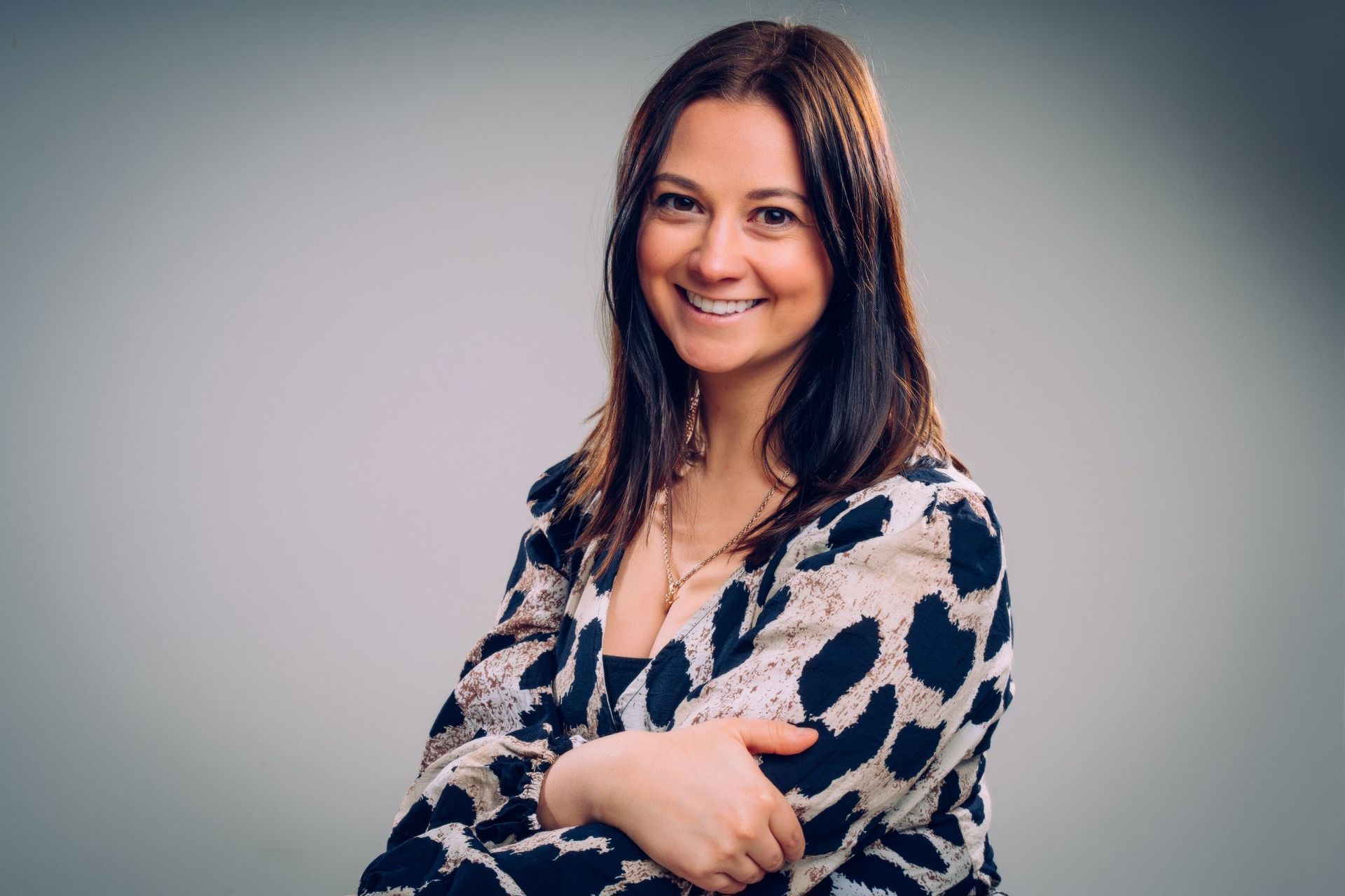 A woman in a leopard print shirt is smiling with her arms crossed.