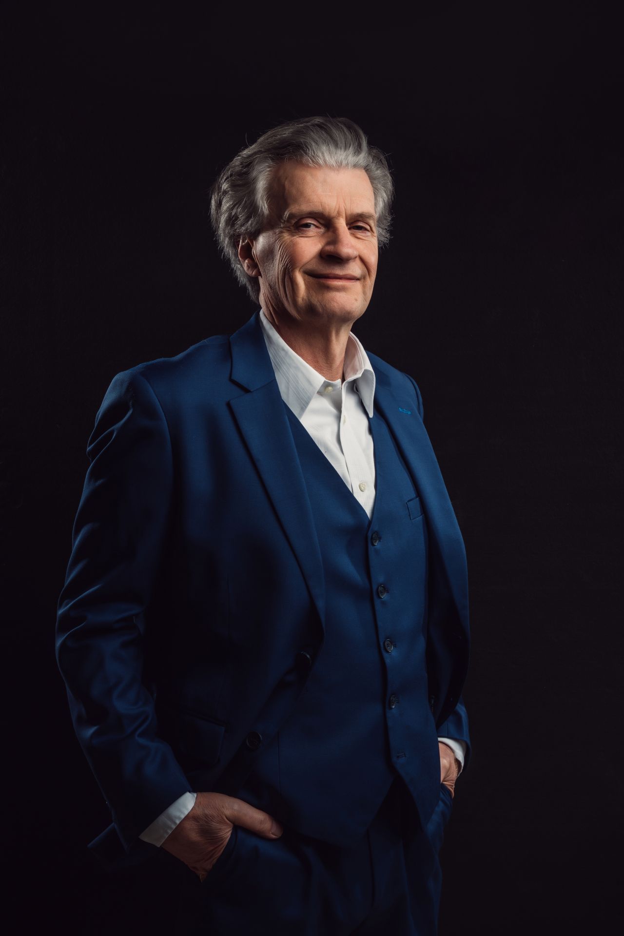 A man in a blue suit and white shirt is standing with his hands in his pockets.