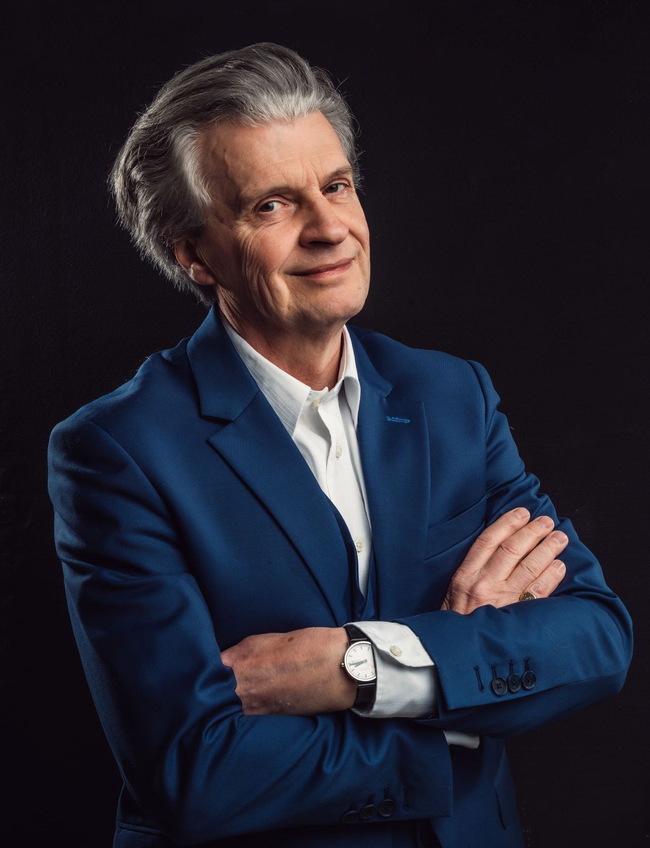 A man in a blue suit and white shirt is standing with his arms crossed.