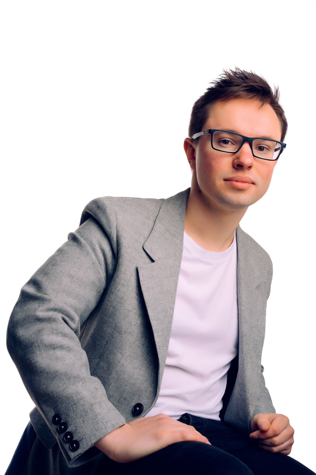A man wearing glasses and a grey jacket is sitting on a chair.
