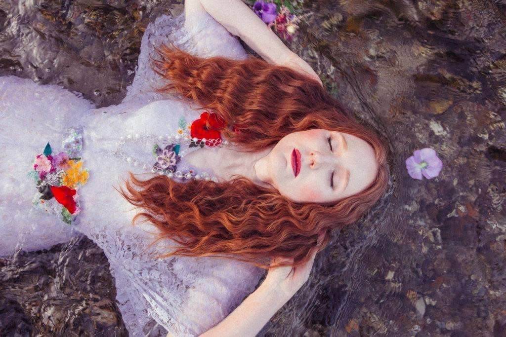 A woman in a white dress is laying on a rock with flowers in her hair.